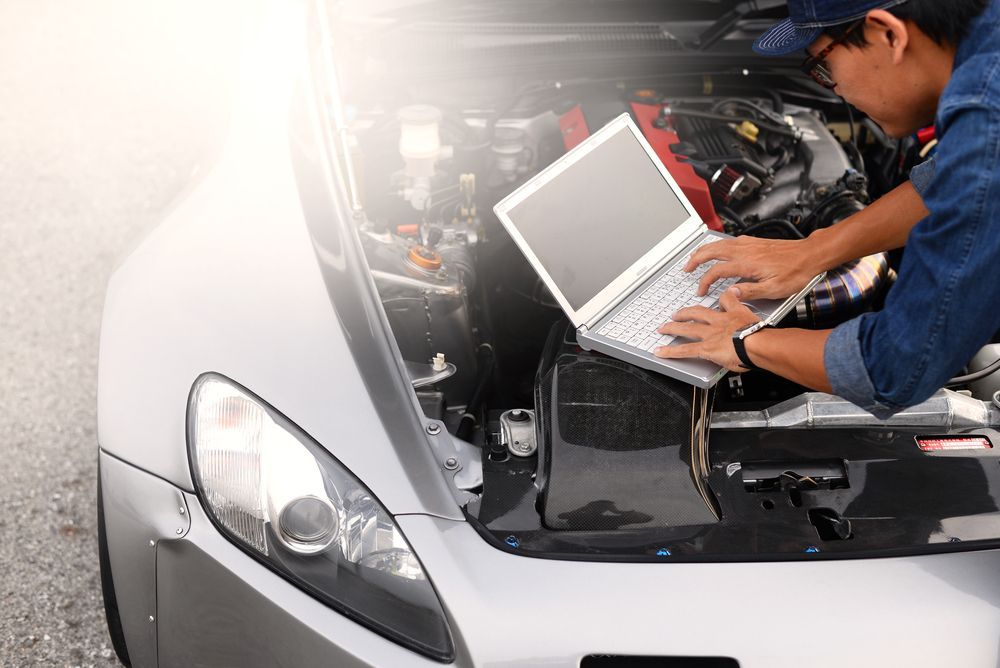 A Man is Working on the Engine of a Car With a Laptop — CJ's Holden Spares & Repairs in Queanbeyan West, NSW