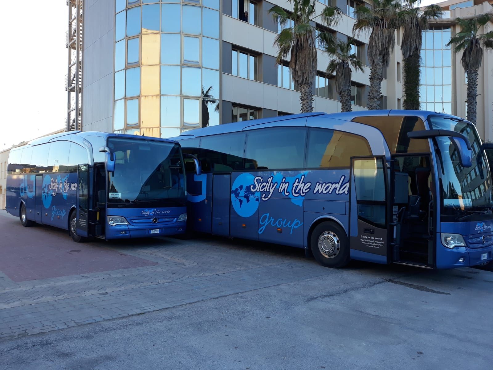 Due autobus blu sono parcheggiati davanti a un edificio che dice