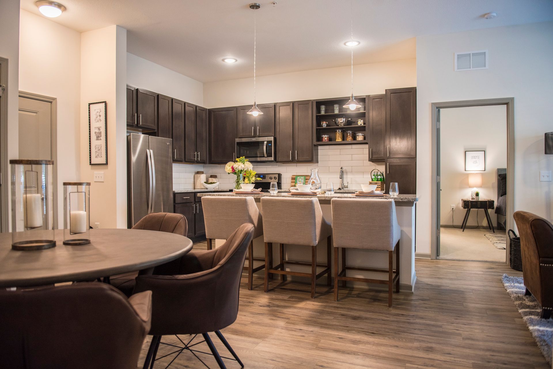 Open-concept kitchen and dining area: dark cabinetry, stainless steel appliances, neutral tones, island seating, round dining table.