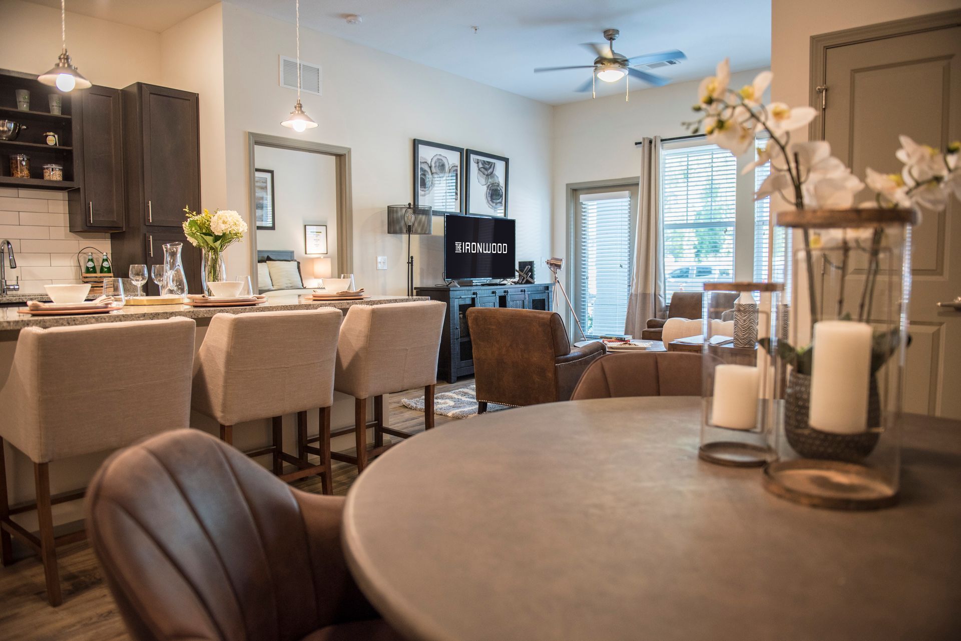 Interior of a well-lit living space with kitchen and dining area. Neutral color scheme, with focus on furniture and decor.