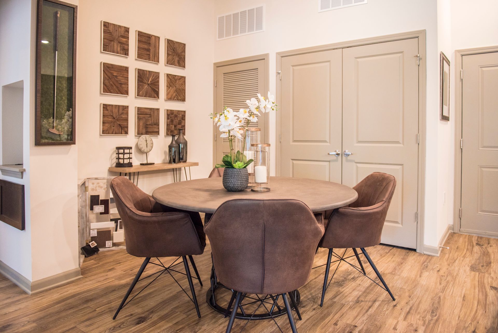 Dining area with round table, four brown chairs, decorative wall art, and flowers.