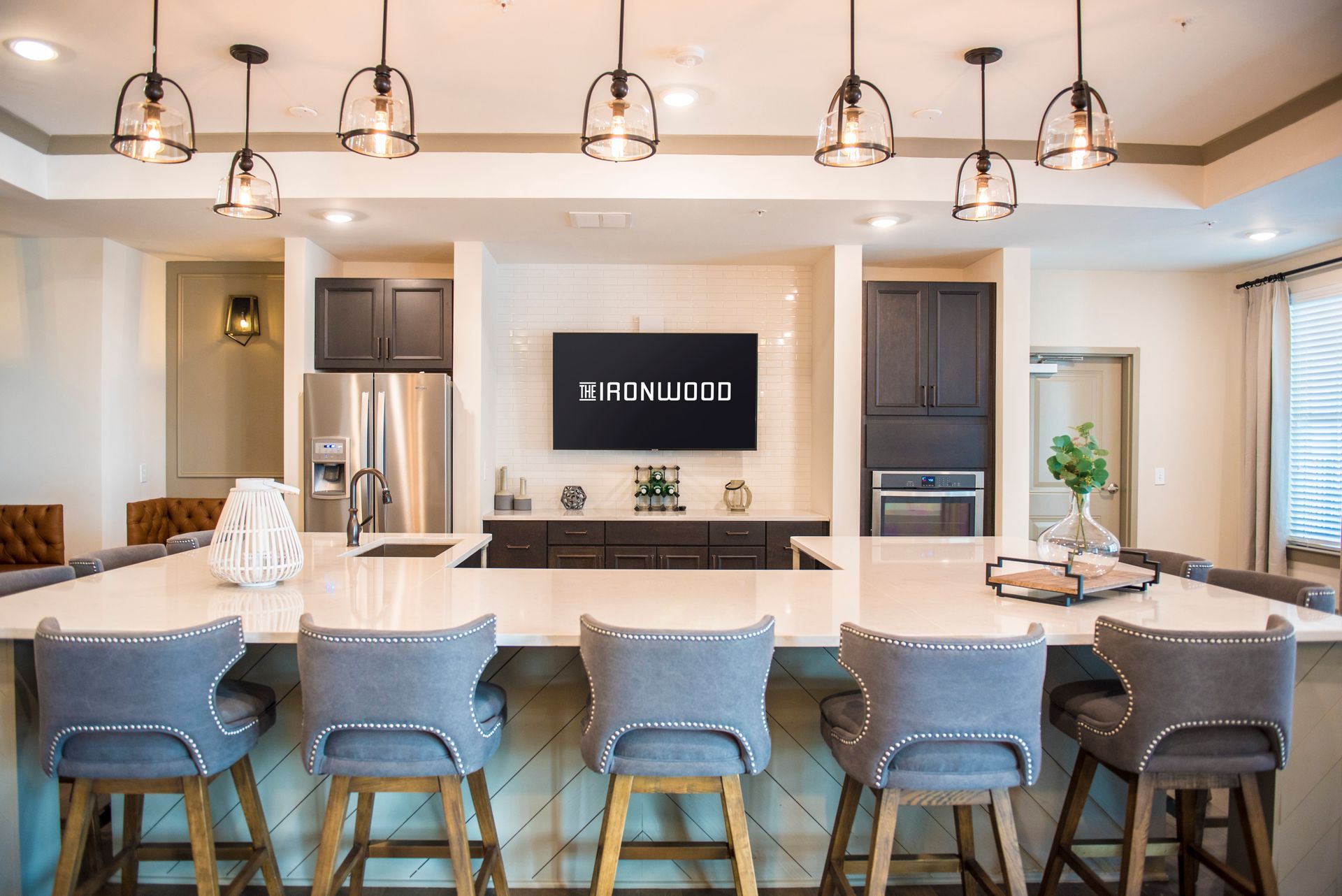 Kitchen with large island, pendant lights, bar stools, and entertainment area with TV.