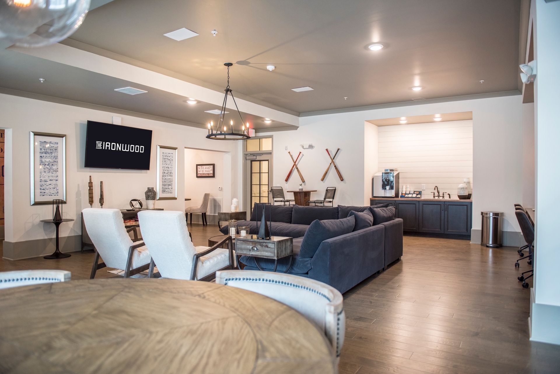 Spacious lounge with couches, armchairs, coffee station, TV, and decorative items. Grey, blue, and white colors.