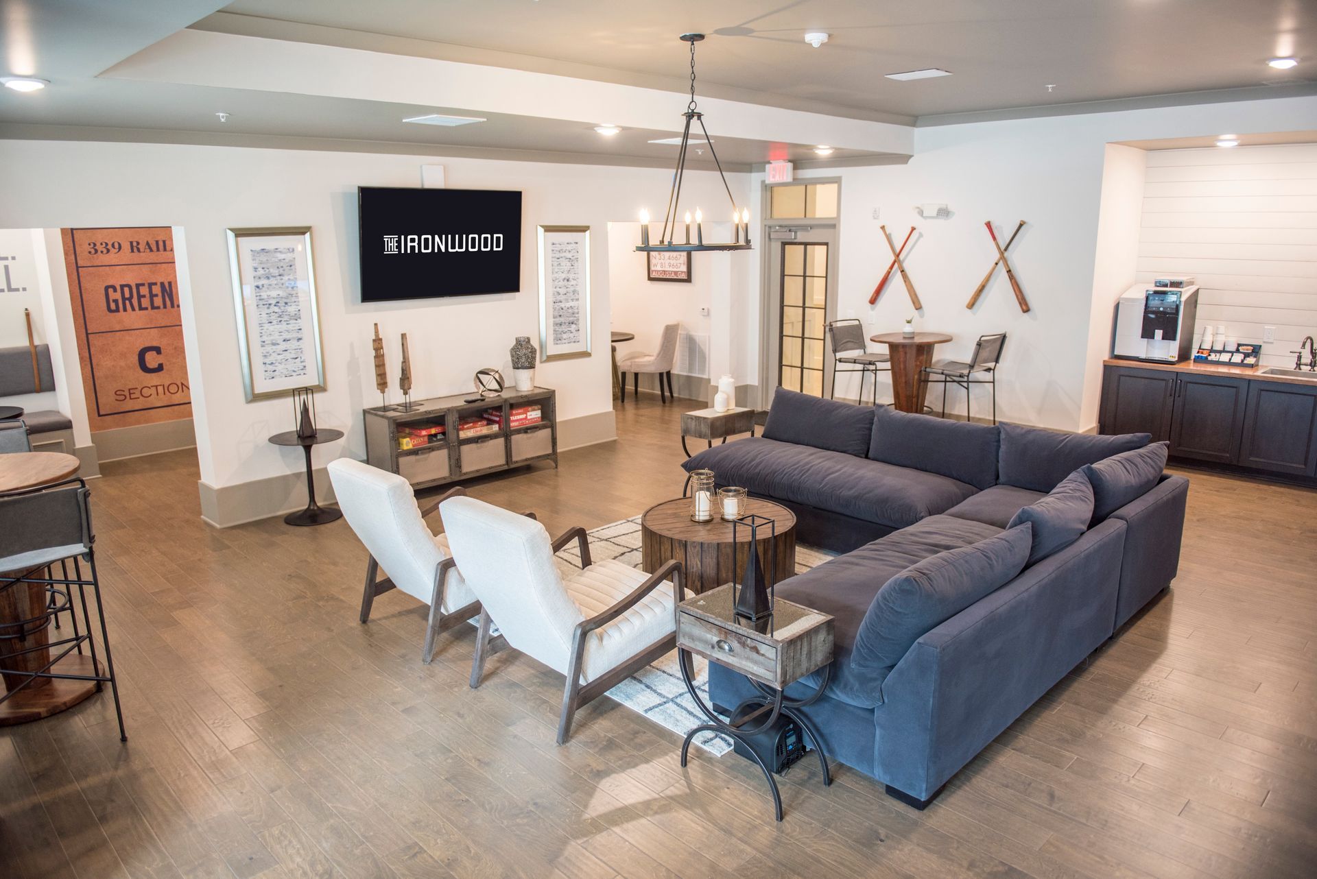 Spacious living area with blue sectional sofa, two white chairs, TV, and coffee station.