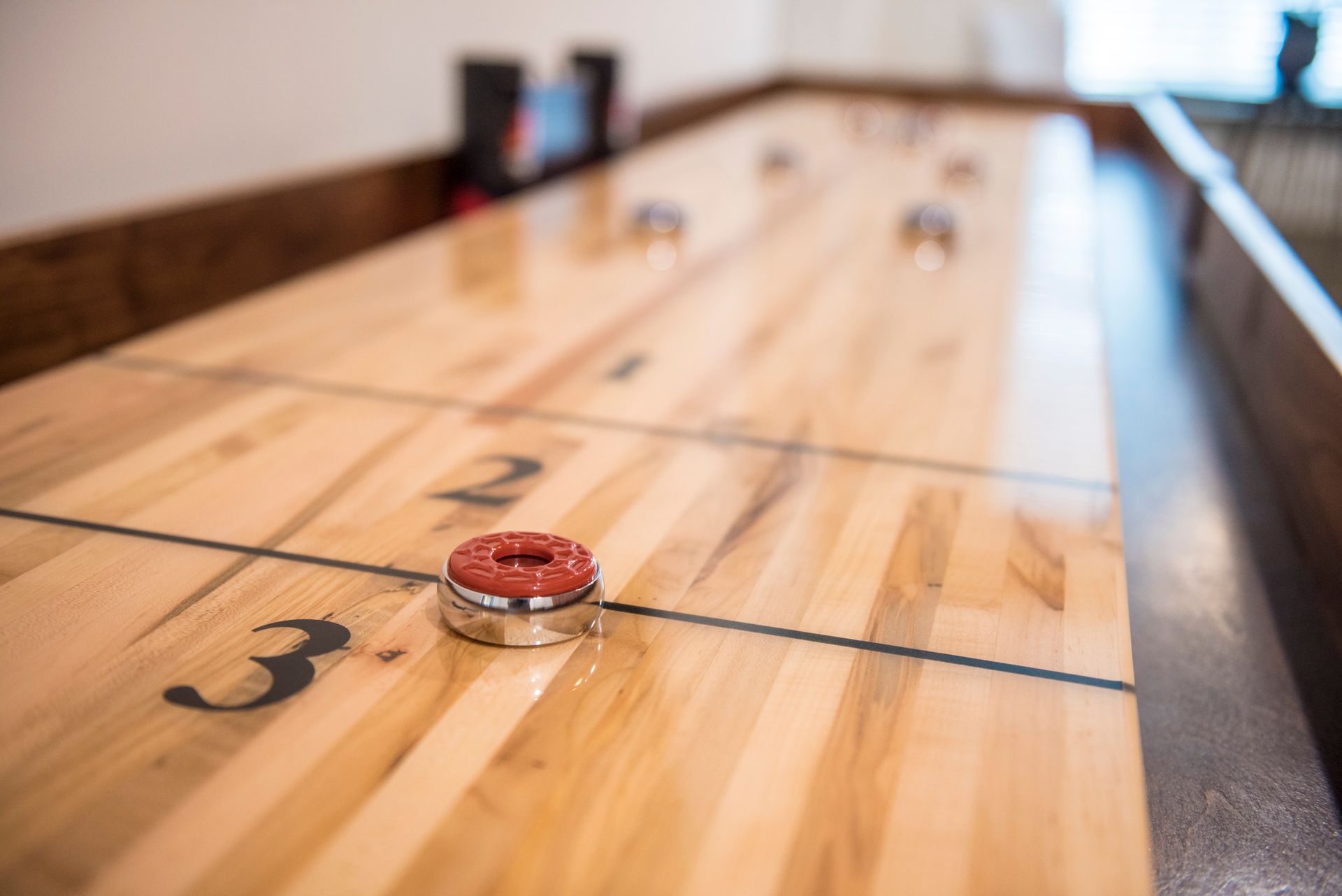 A shuffleboard table with red puck in foreground and other pucks further down.