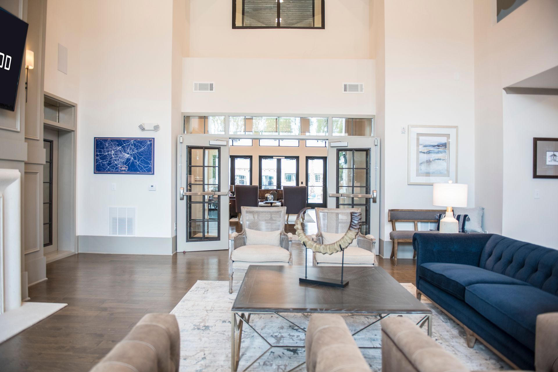 Spacious lobby with blue sofa, armchairs, coffee table, art, and doors to an exterior.