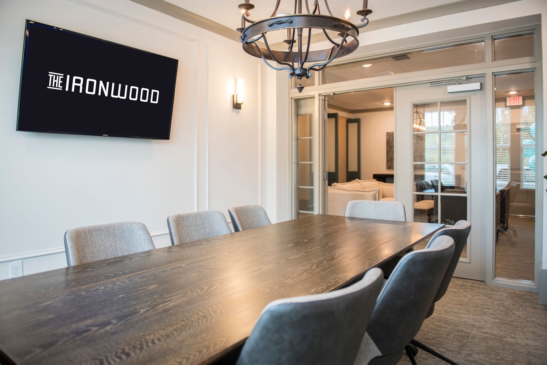 Conference room with long wooden table, gray chairs, TV with