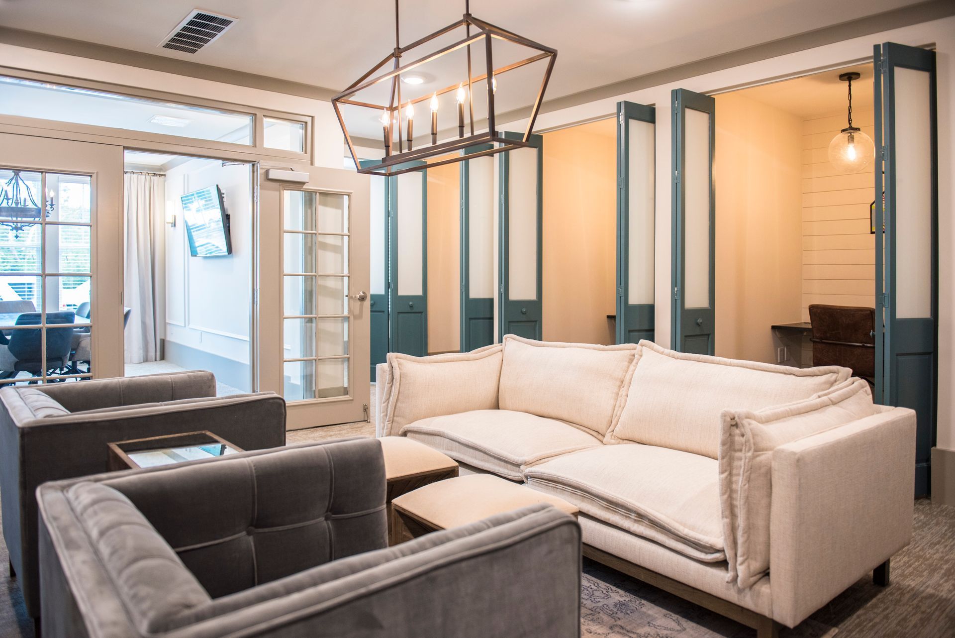 Living room with sofa, chairs, and doors, with an open door to a room with a desk.