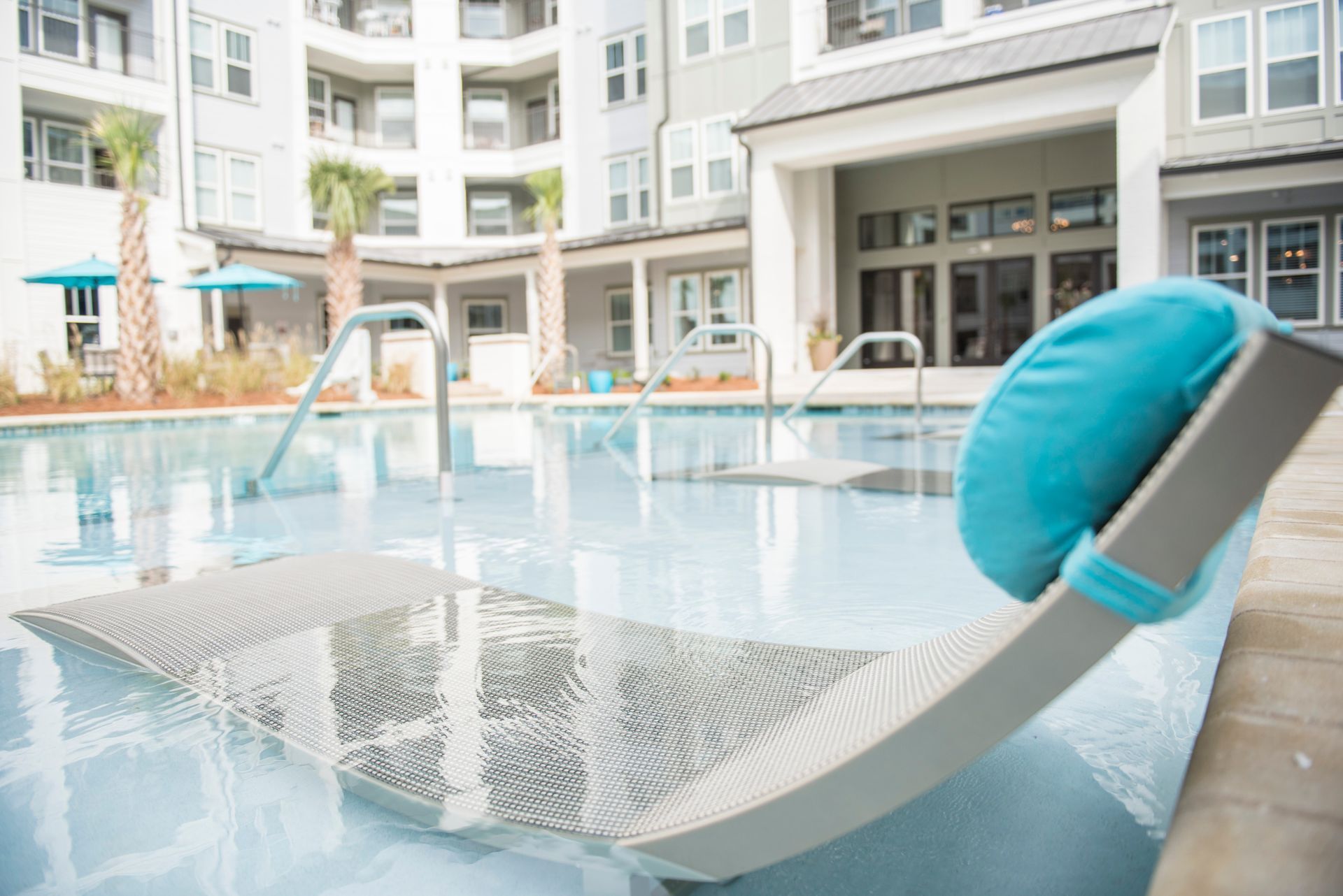 Lounge chair with turquoise pillow by a pool at an apartment complex.