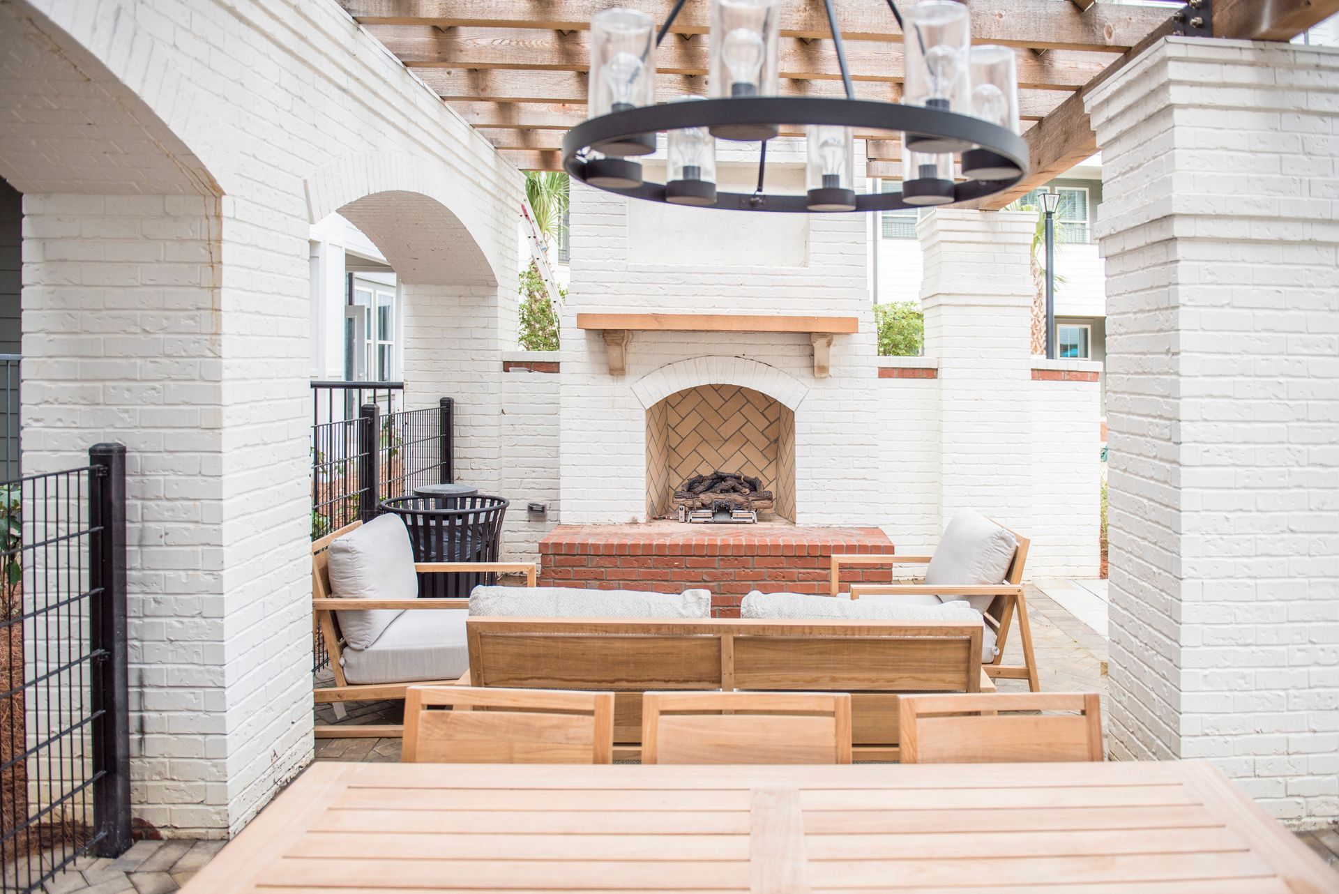 Outdoor patio with white brick, fireplace, wooden furniture, and black chandelier.