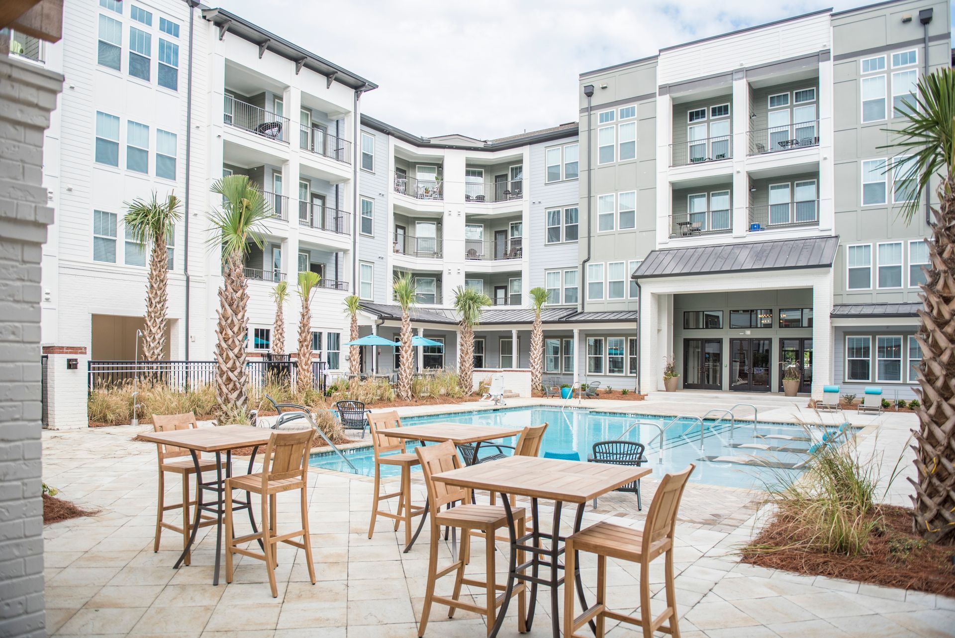 Outdoor pool area with tables, chairs, and multiple story apartment buildings.