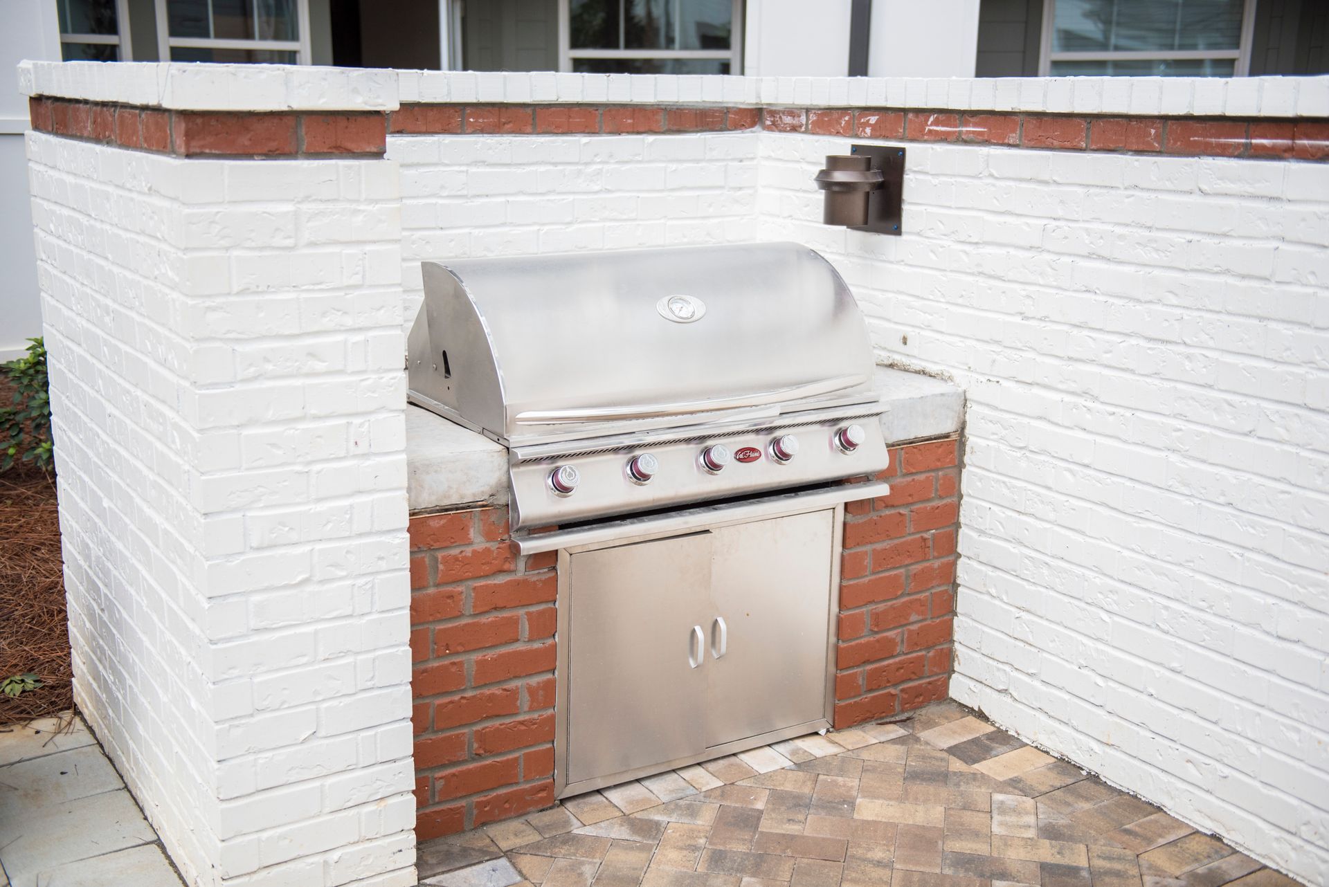 Brick-built outdoor kitchen with a stainless steel grill. White-painted brick walls frame the red brick base.