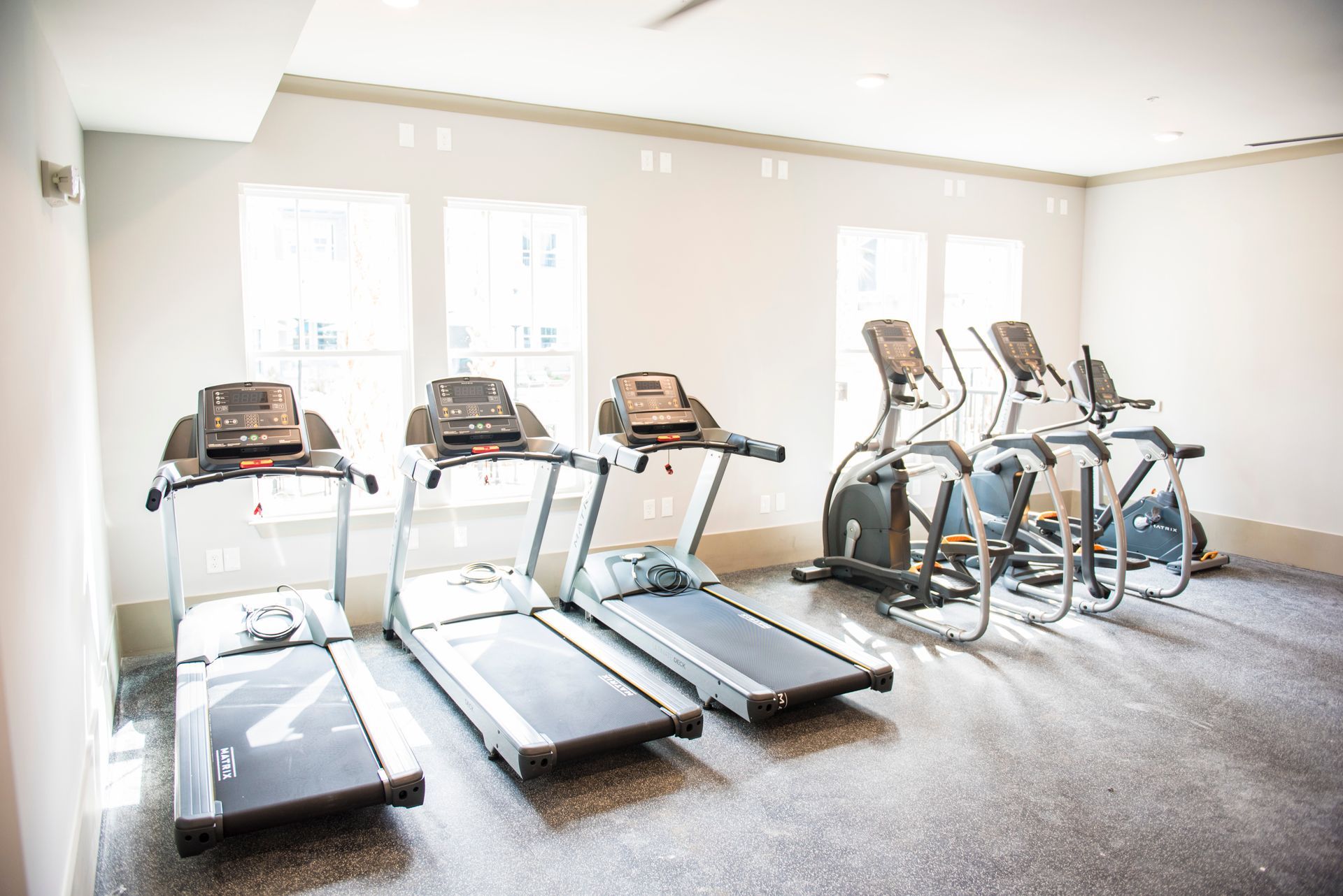 Gym with three treadmills and two elliptical machines by a window.