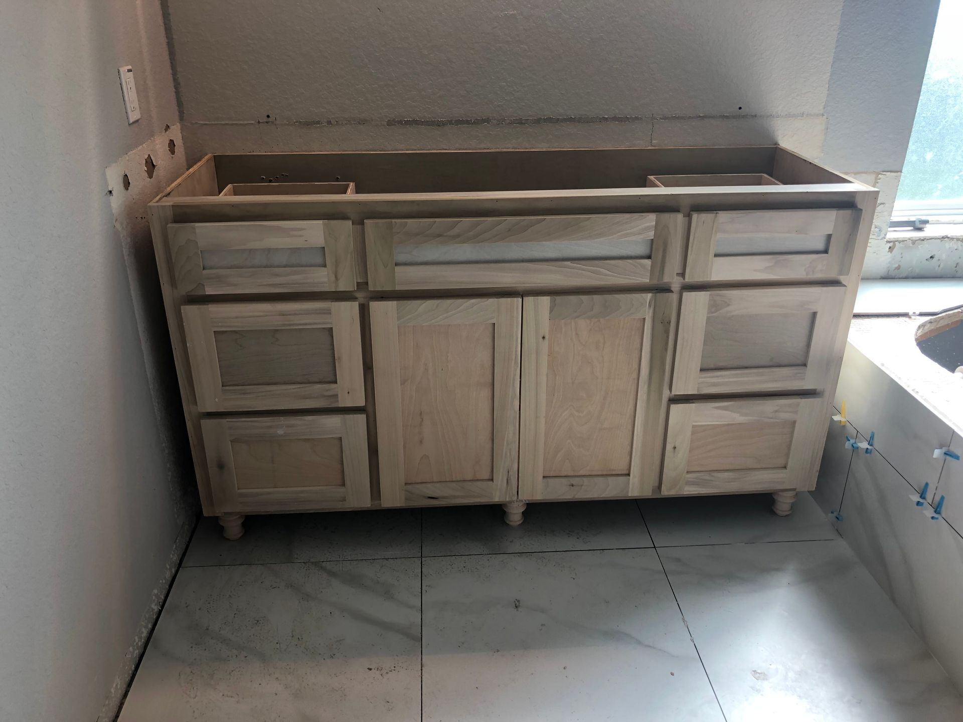 An unfinished wooden bathroom vanity cabinet installed on a tile floor in an incomplete room.