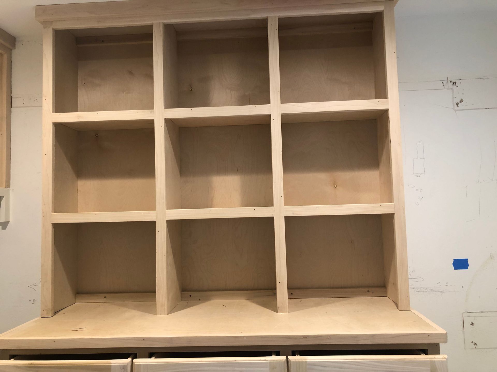 A wooden, unfinished nine-cube shelving unit mounted on a wall.