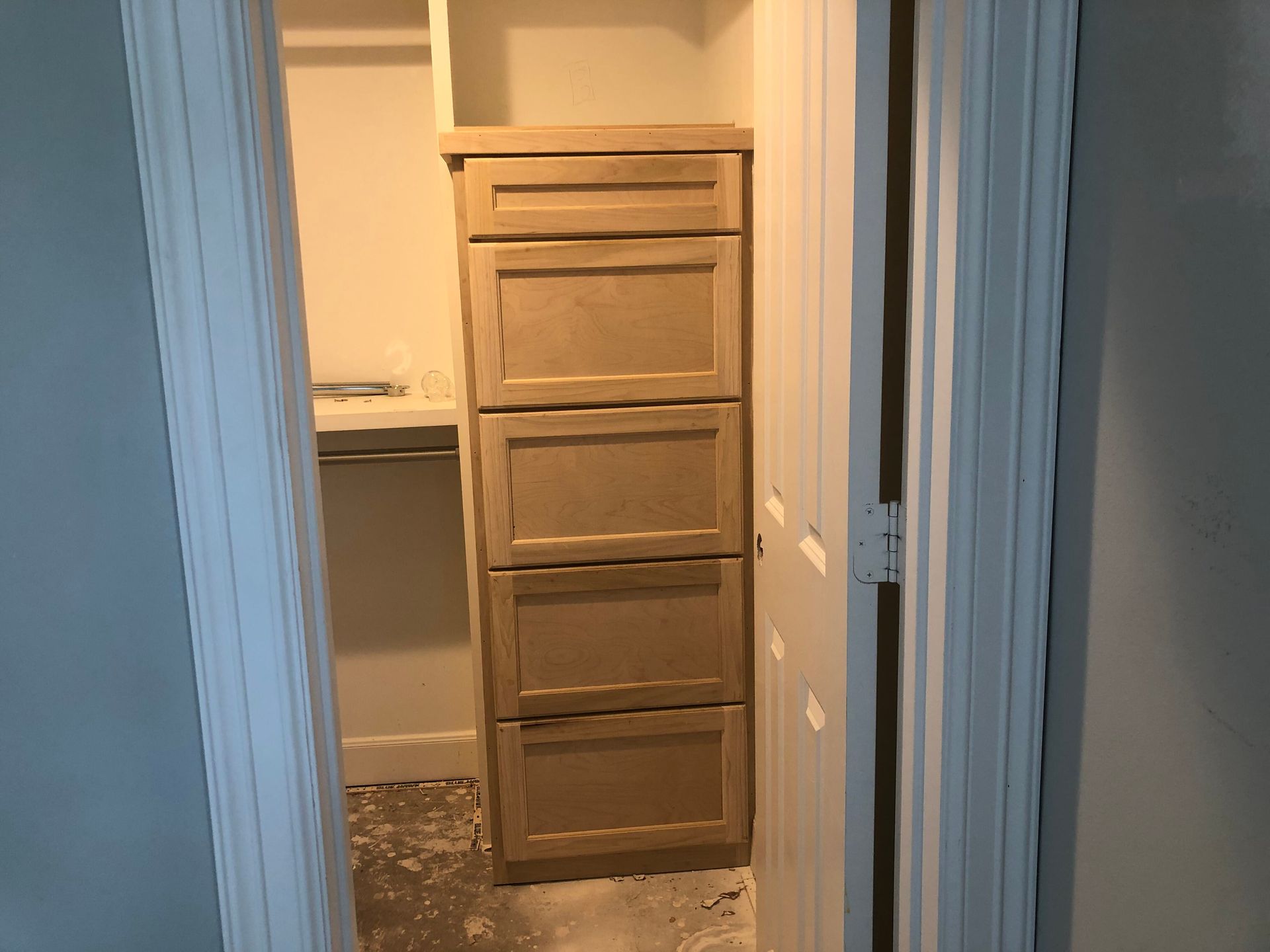 A light-colored wooden chest of drawers installed inside a closet doorway next to a white door.