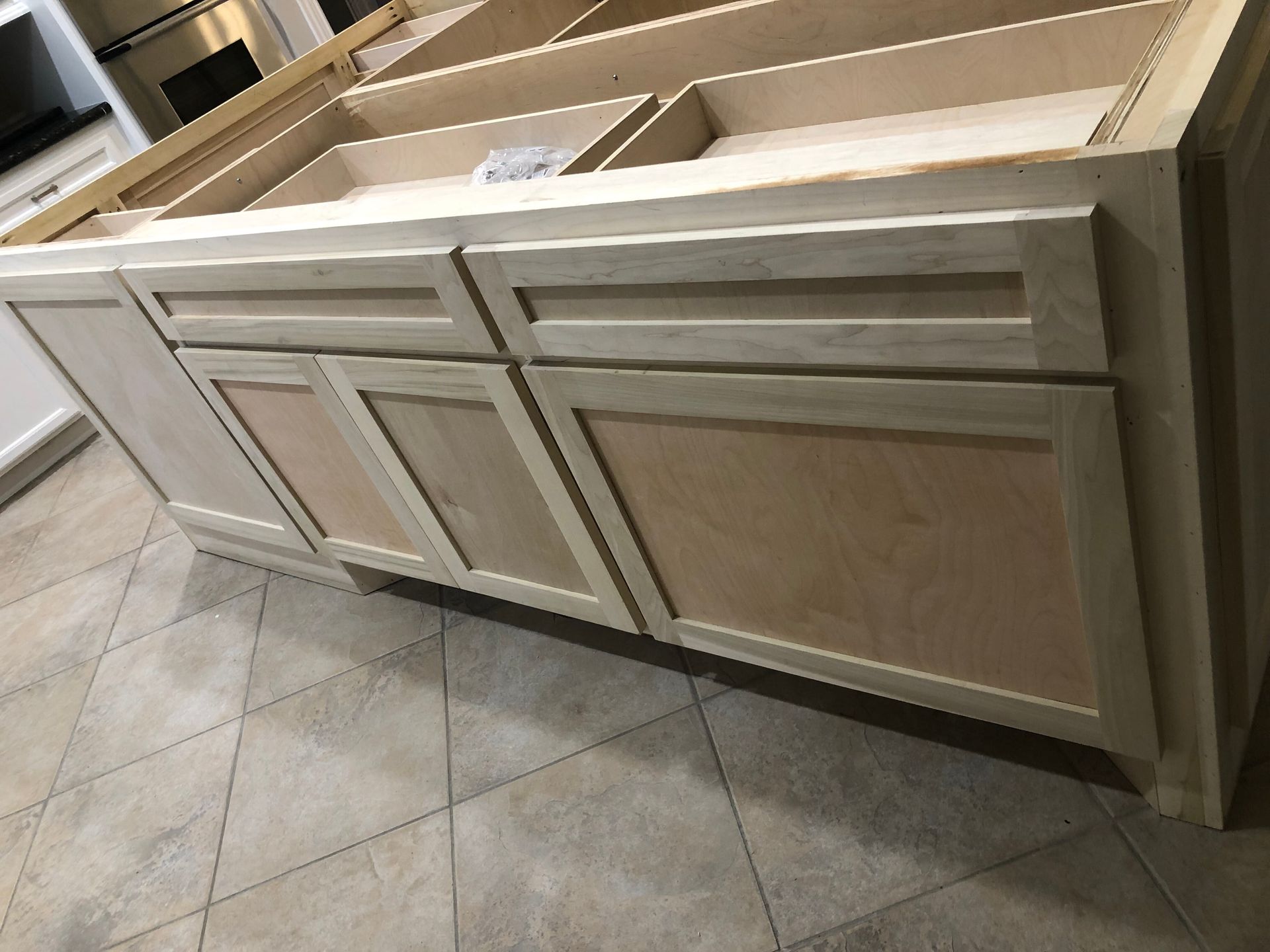 Unfinished wooden kitchen island base with drawers and cabinet doors, positioned on a tiled floor.