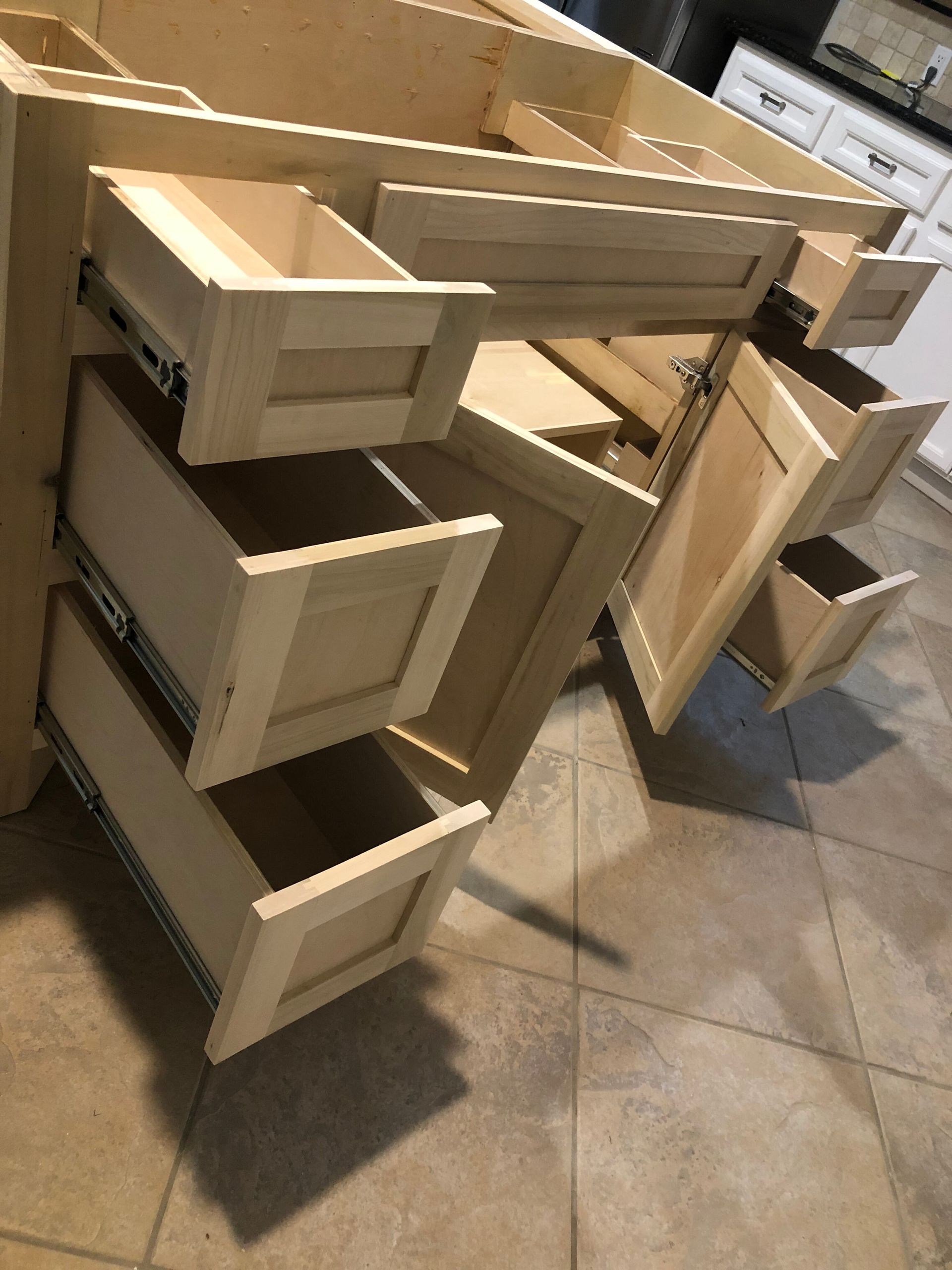 An unfinished wooden bathroom vanity cabinet with several drawers pulled open, sitting on a tiled floor.