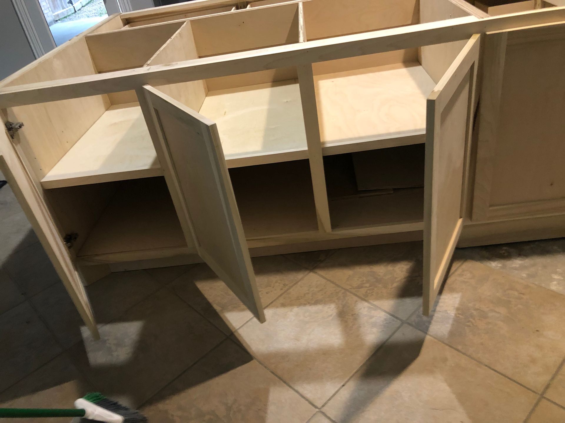 An unfinished wooden cabinet with open doors and exposed interior shelves, sitting on a tiled floor in a room.