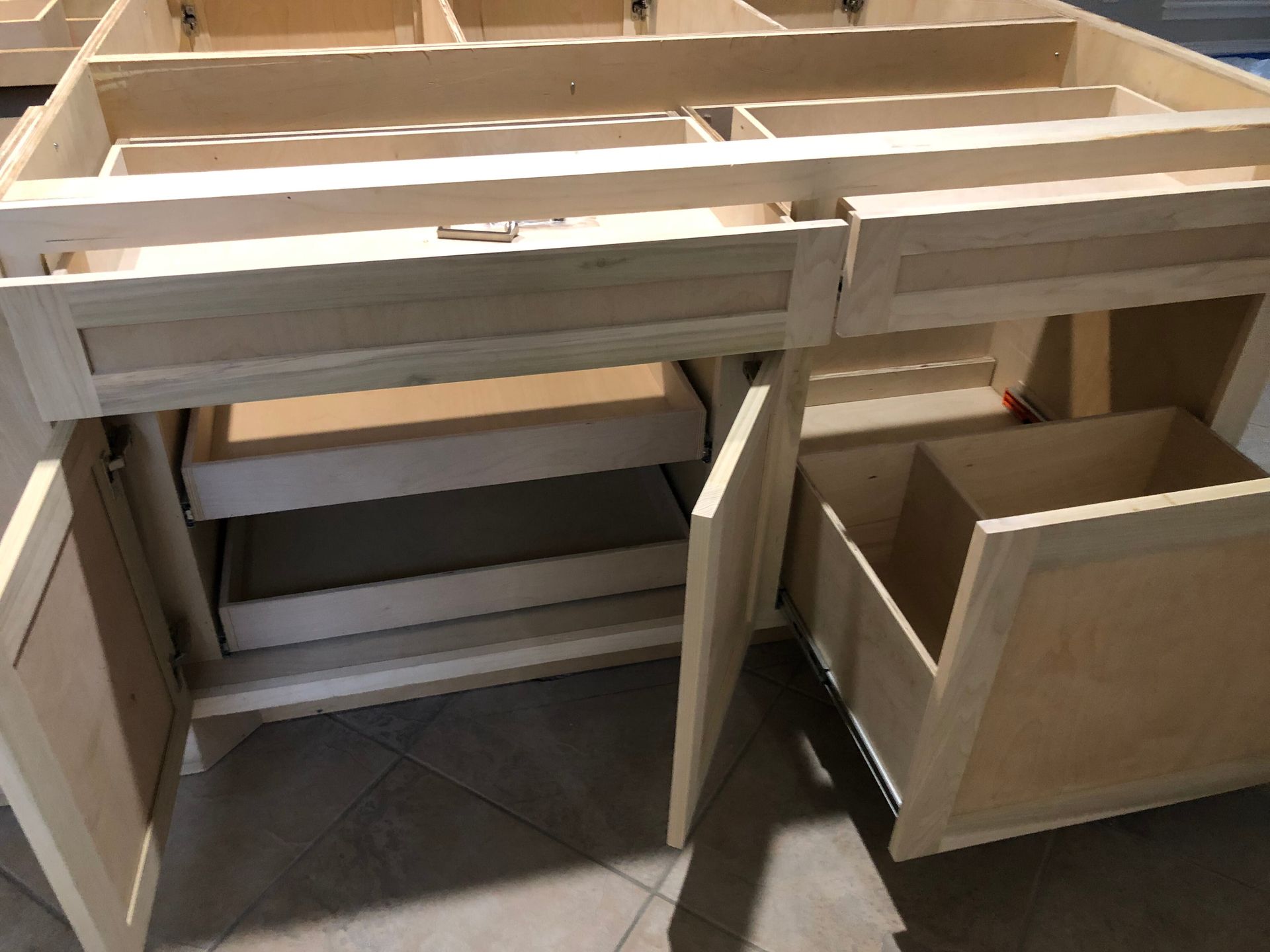 A wooden kitchen cabinet base with two open doors, two pull-out interior shelves, and a large pull-out trash drawer.