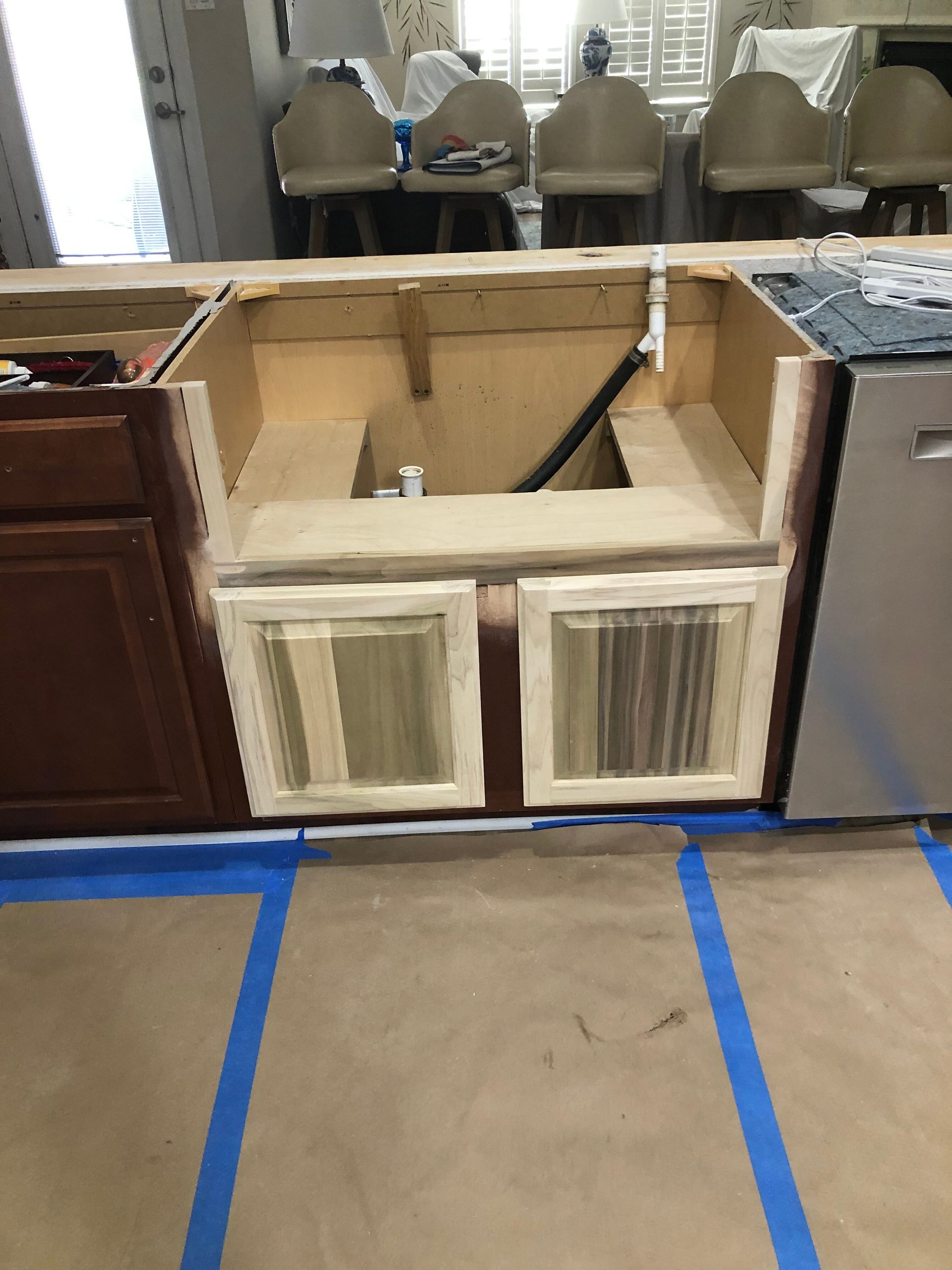 A kitchen island under construction with an empty sink cutout, exposed wood frame, and protective floor paper.
