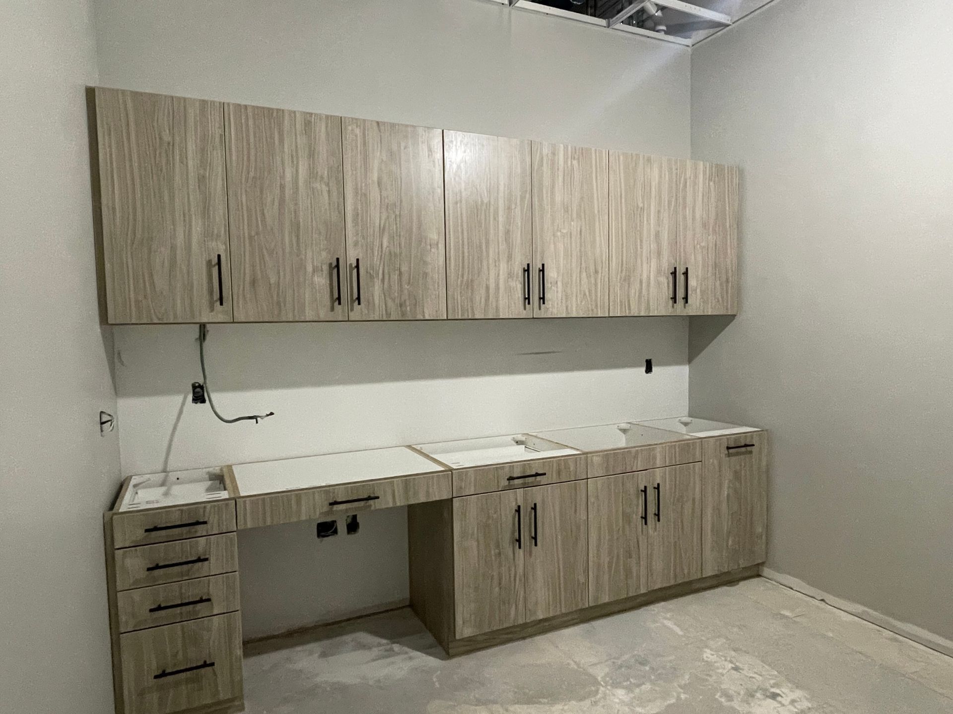Light wood grain cabinets and drawers installed on a pale wall in an unfinished room.