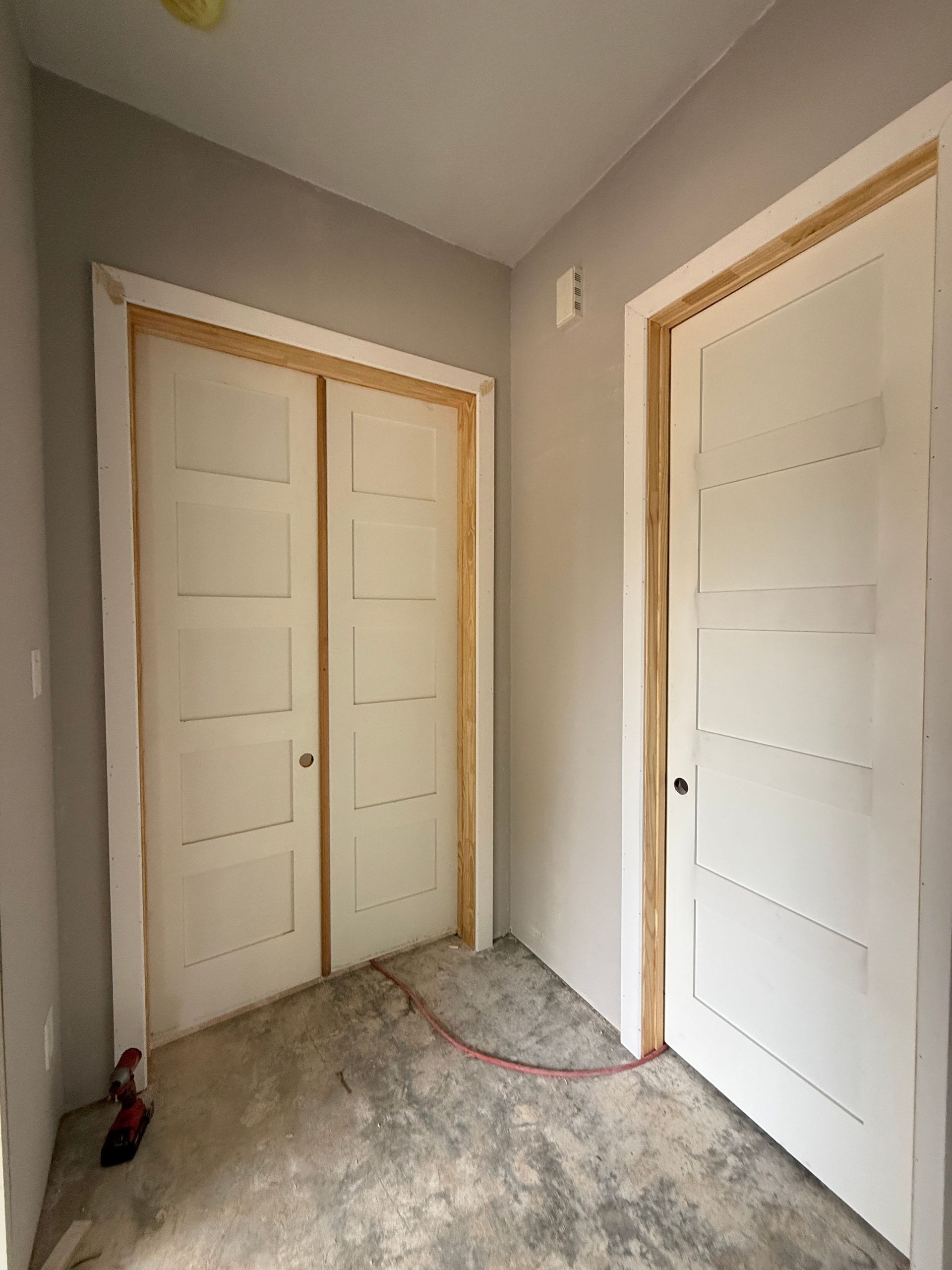 Interior view of a room under construction with two white, five-panel doors, unfinished wood trim, and gray walls.