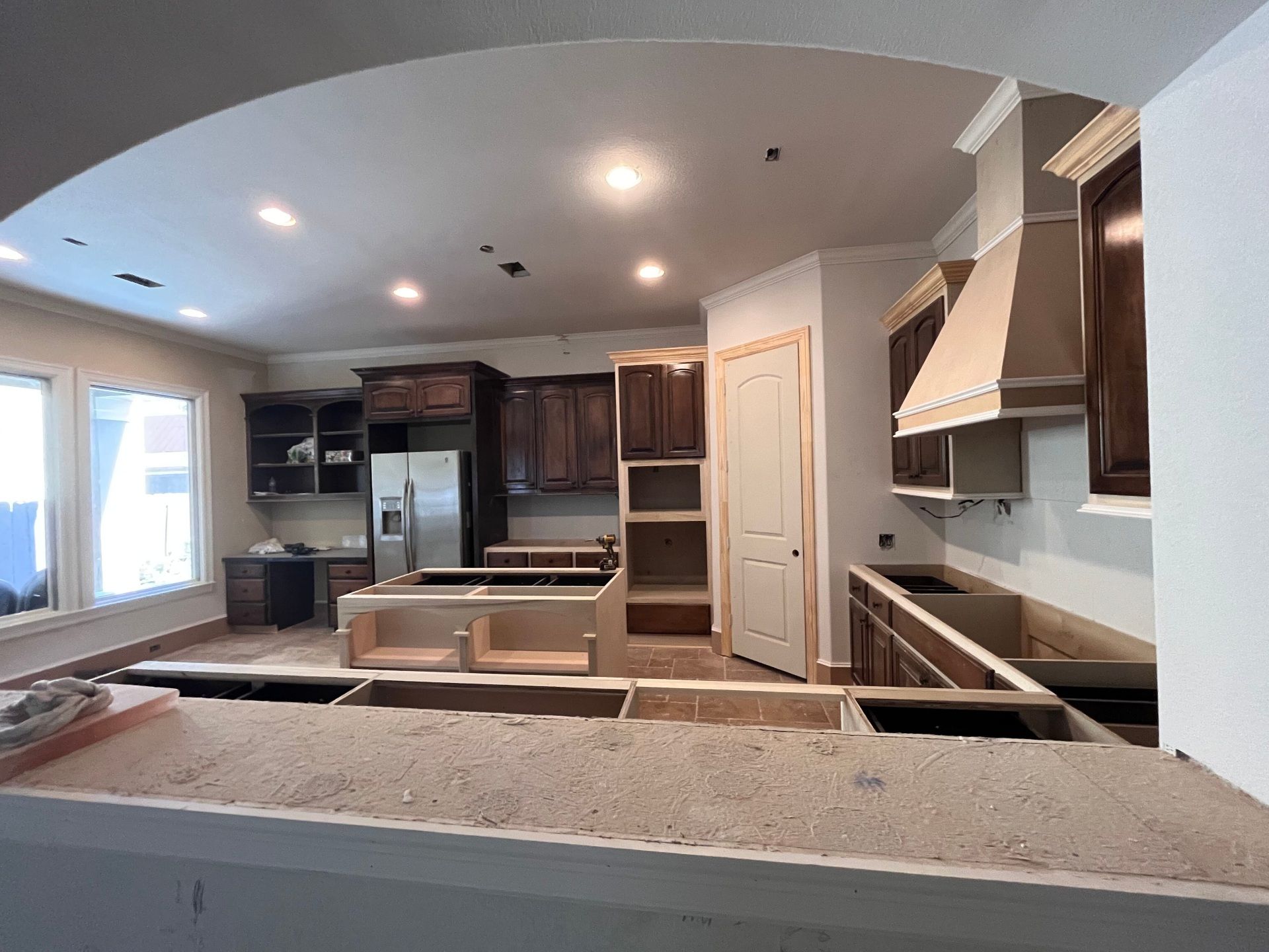 A kitchen in the middle of a renovation with dark wood cabinets, a stainless steel refrigerator, and unfinished counters.