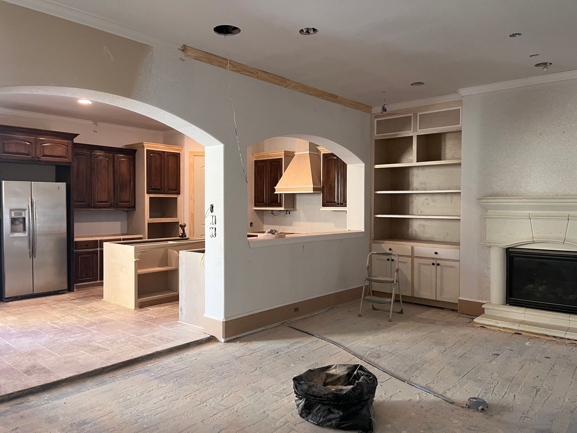 Interior of a room under renovation, showing a kitchen with dark cabinets, a fireplace, and built-in wall shelving.