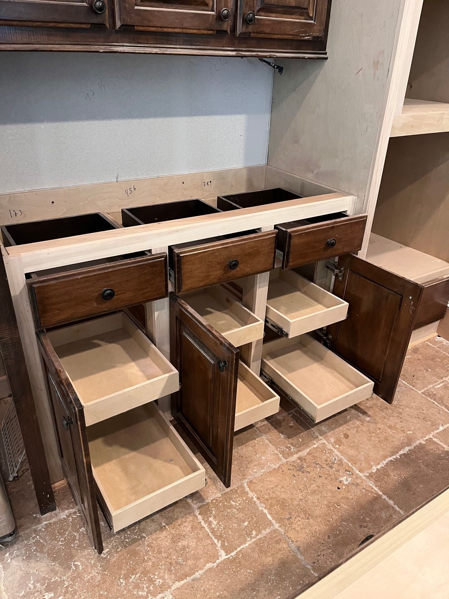 A wooden bathroom vanity with three drawers and pull-out shelves, set against a stone tile floor and unfinished walls.