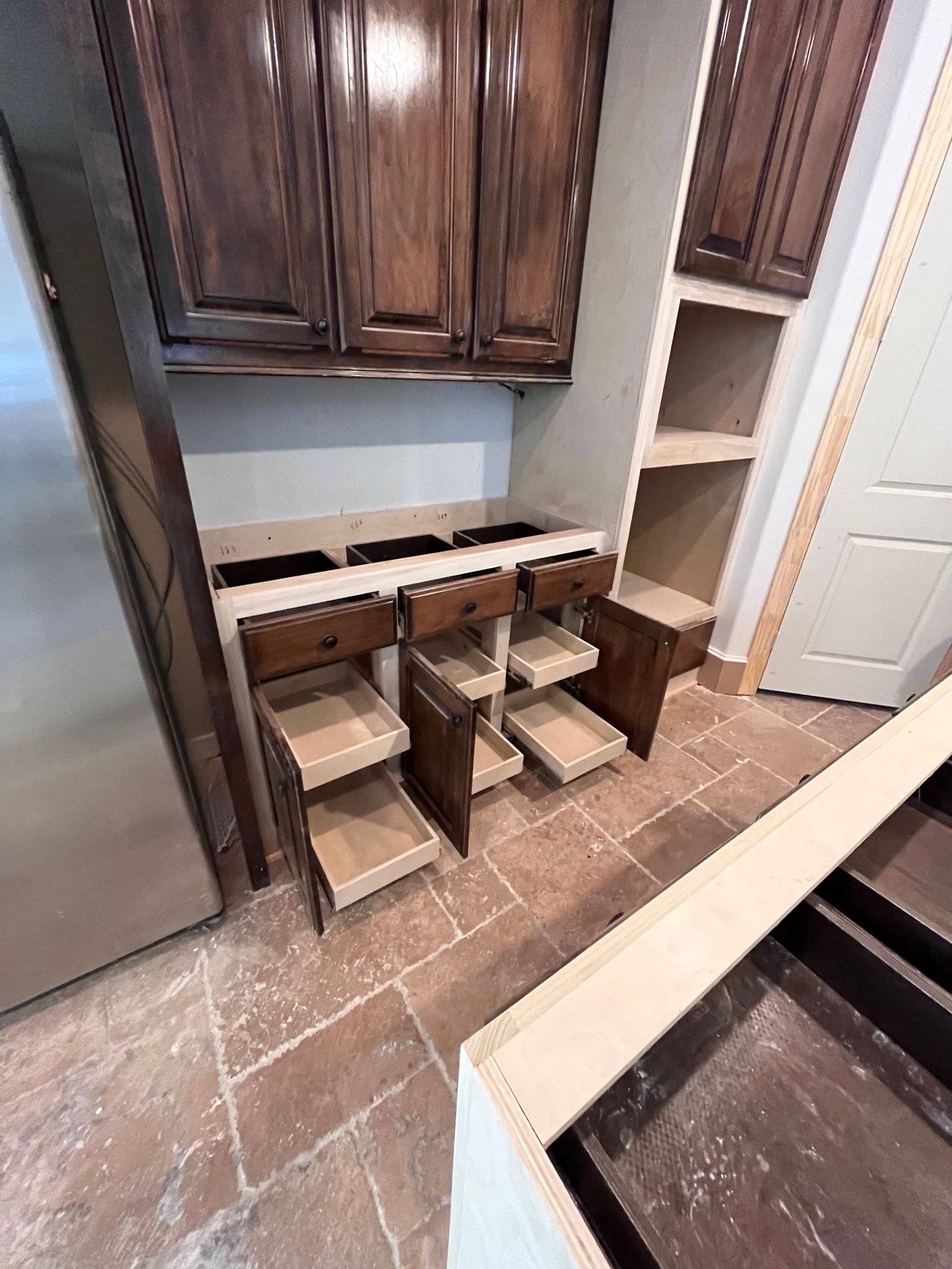 Dark wood cabinets and base units with pull-out drawers installed in a kitchen with tiled floors.