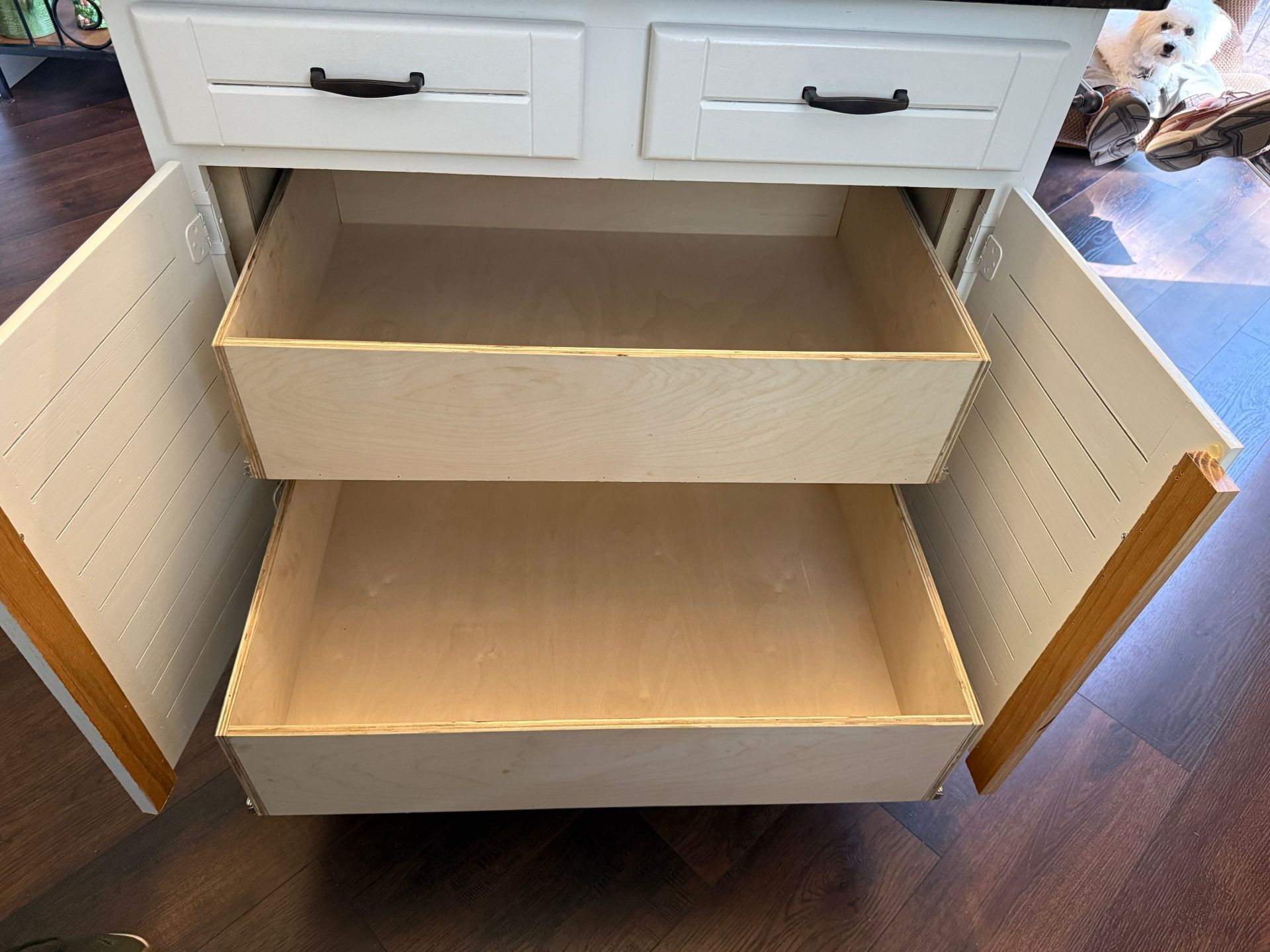 A white kitchen island with two drawers pulled open, revealing empty wooden storage bins and interior shelving.