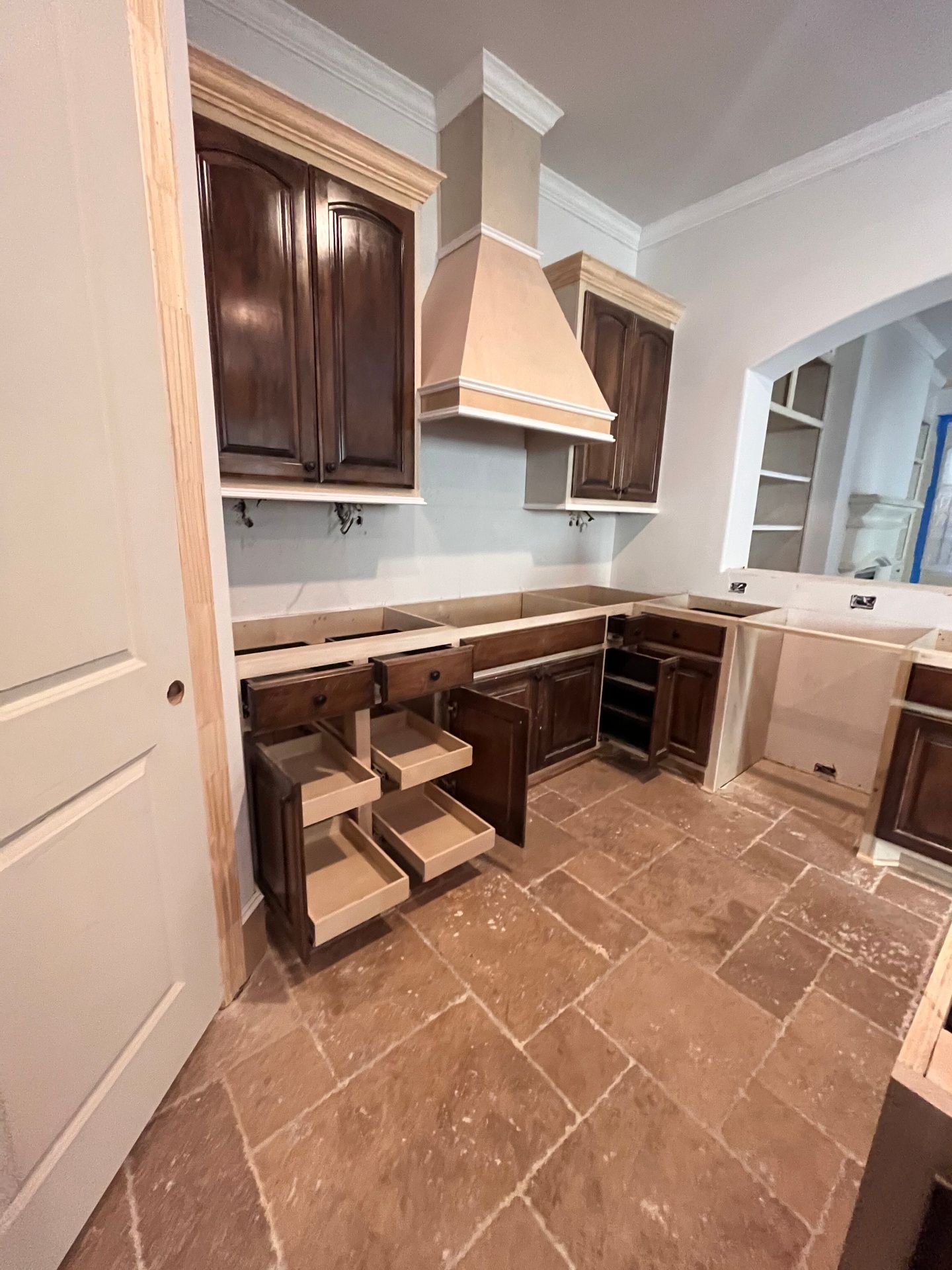A kitchen undergoing renovation with dark wood upper cabinets, a central light-colored range hood, and open base cabinets.