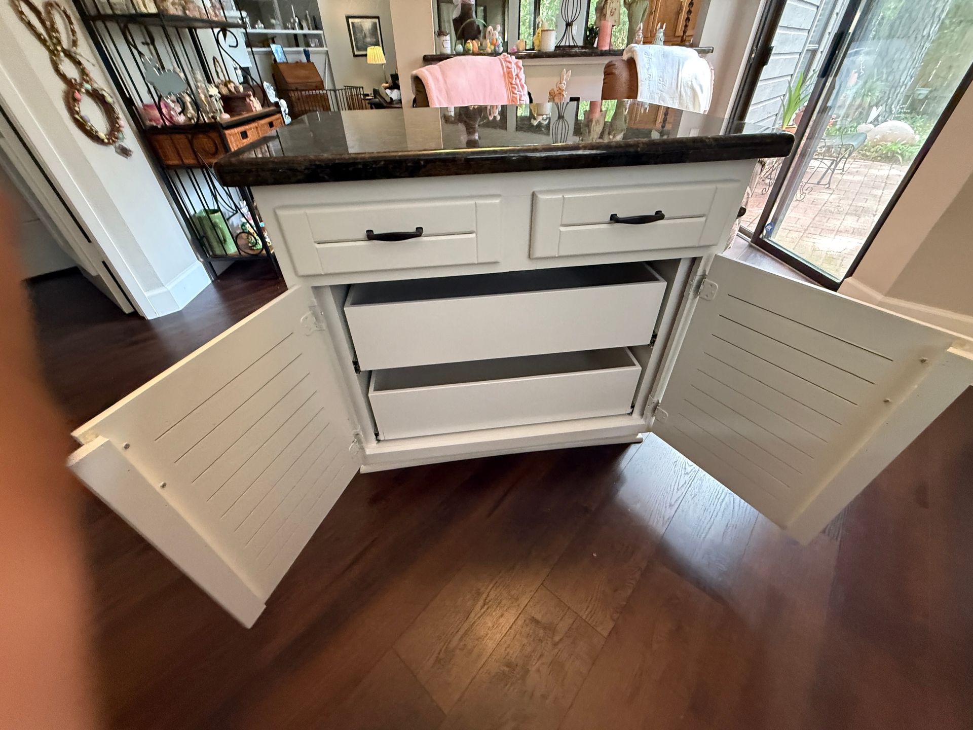 A white kitchen island with two drawers on top and two open, empty white shelves below, set on a dark wood floor.