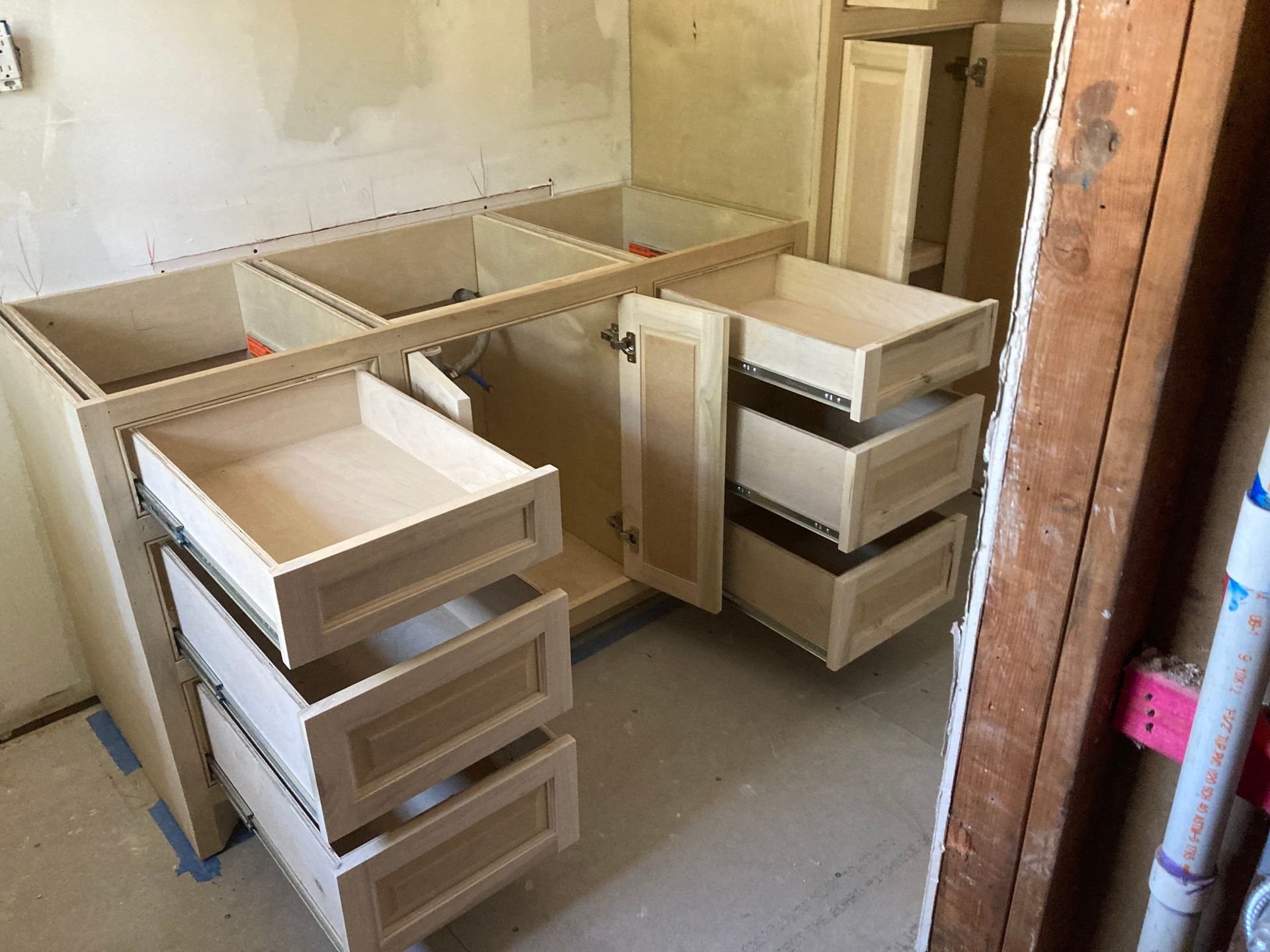 Light-colored wood bathroom vanity base cabinets installed in a room under construction with drawers and doors open.