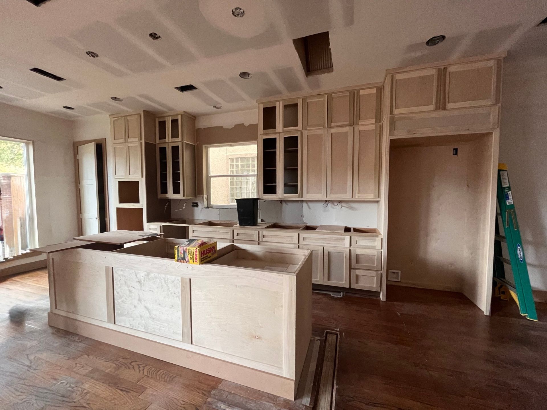 An unfinished kitchen with light wood cabinetry, a center island, and installed flooring under a ceiling with cutouts.