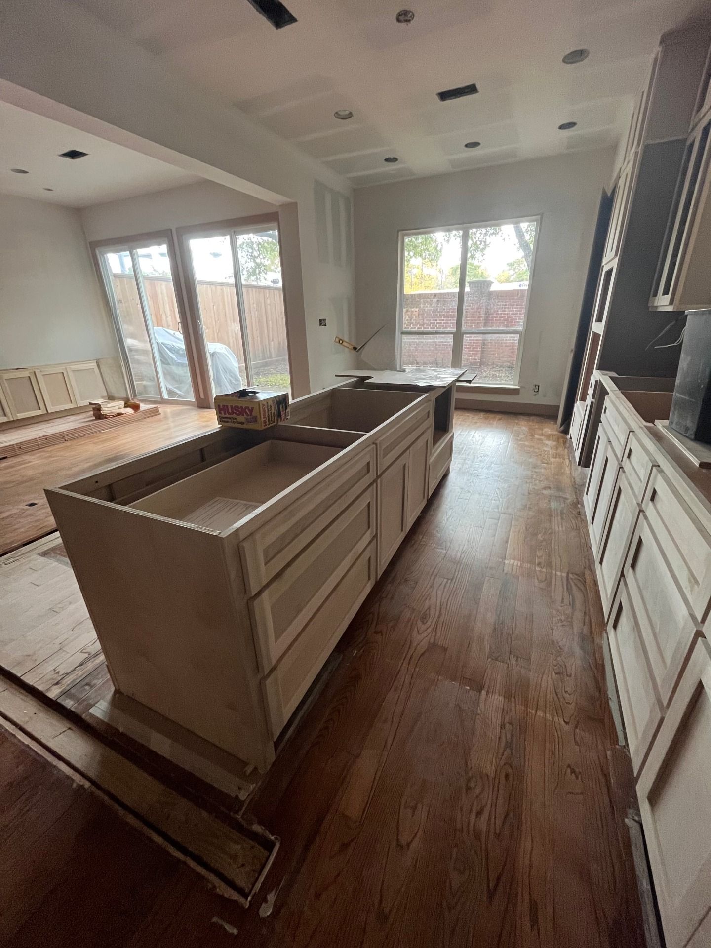 Unfinished kitchen remodel featuring light wood cabinetry, a central kitchen island, and hardwood floors in a sunlit room.