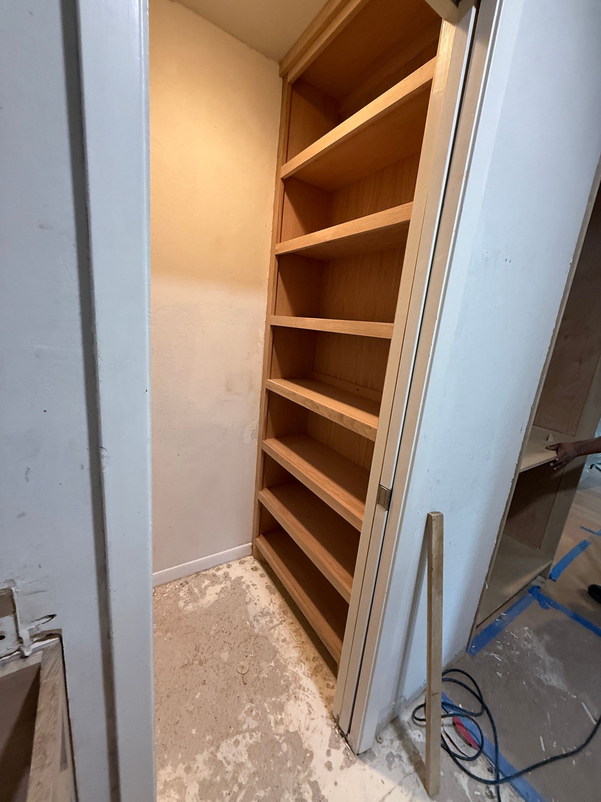 An open doorway reveals a built-in shelving unit with multiple wooden shelves inside a room under construction.