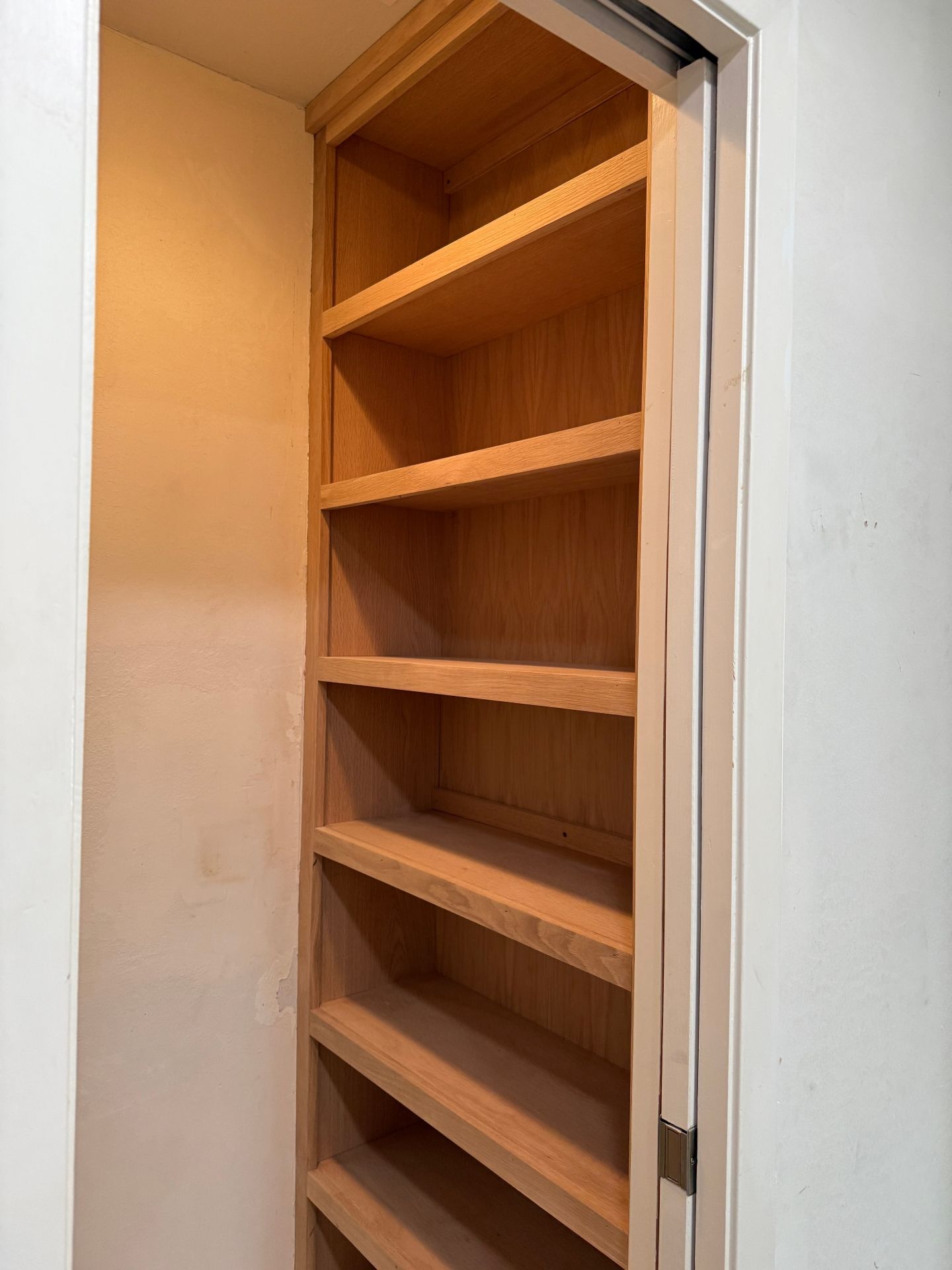 A vertical set of empty, light-colored wooden shelves installed inside a narrow wall alcove.