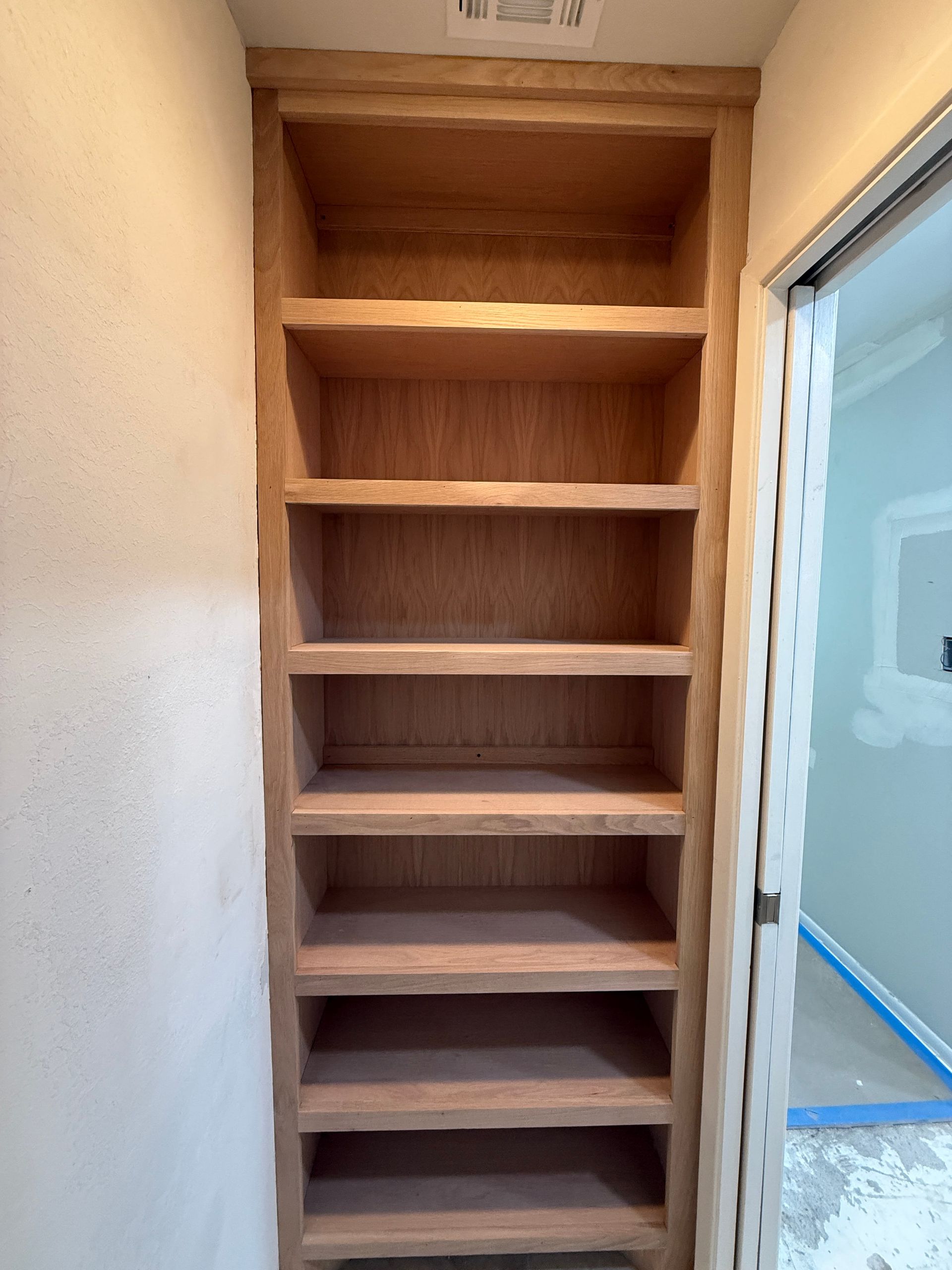 A built-in set of unfinished wooden shelves recessed into a wall inside a house under renovation.