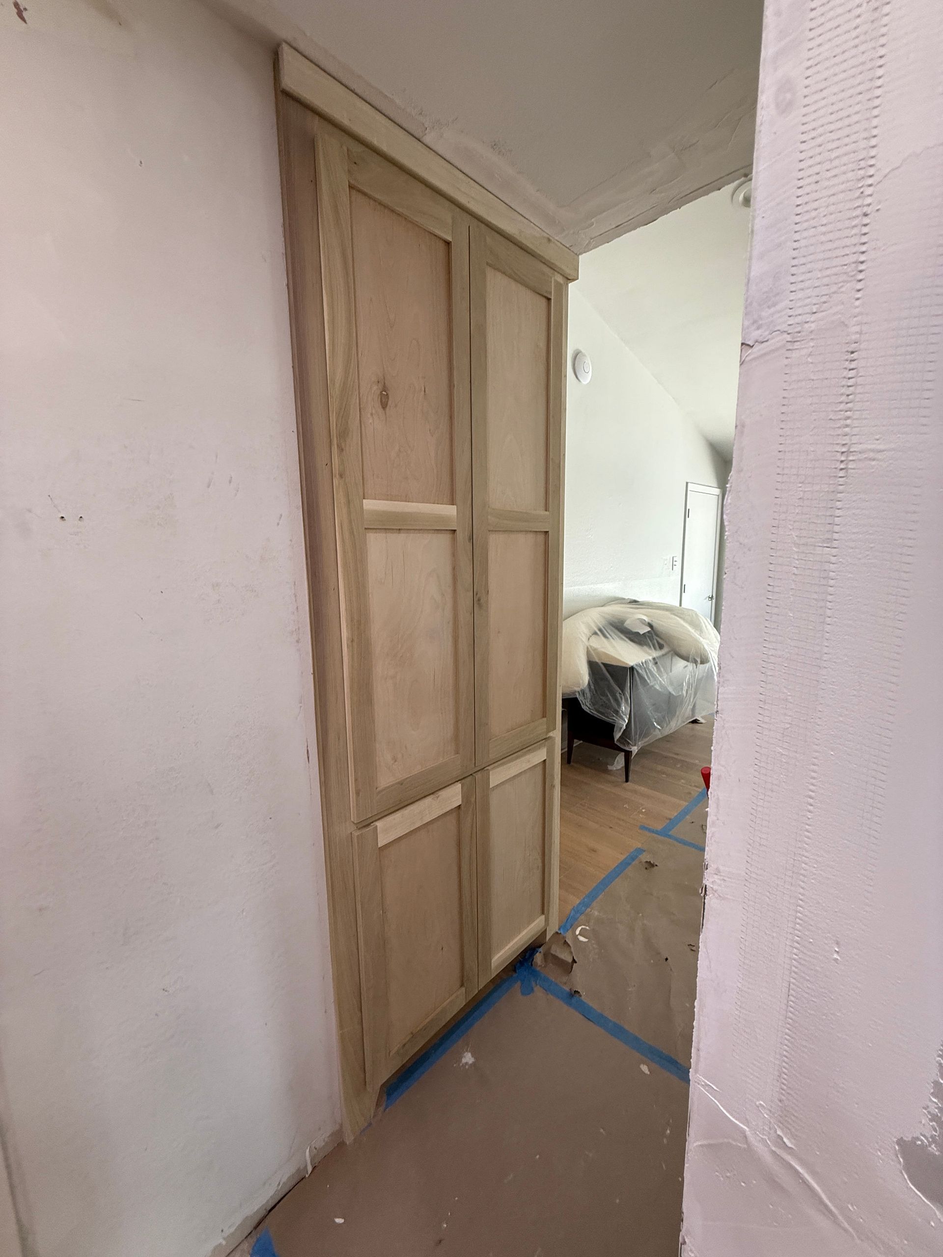Wooden double-door cabinet installed in a recessed wall area with unpainted drywall surroundings.