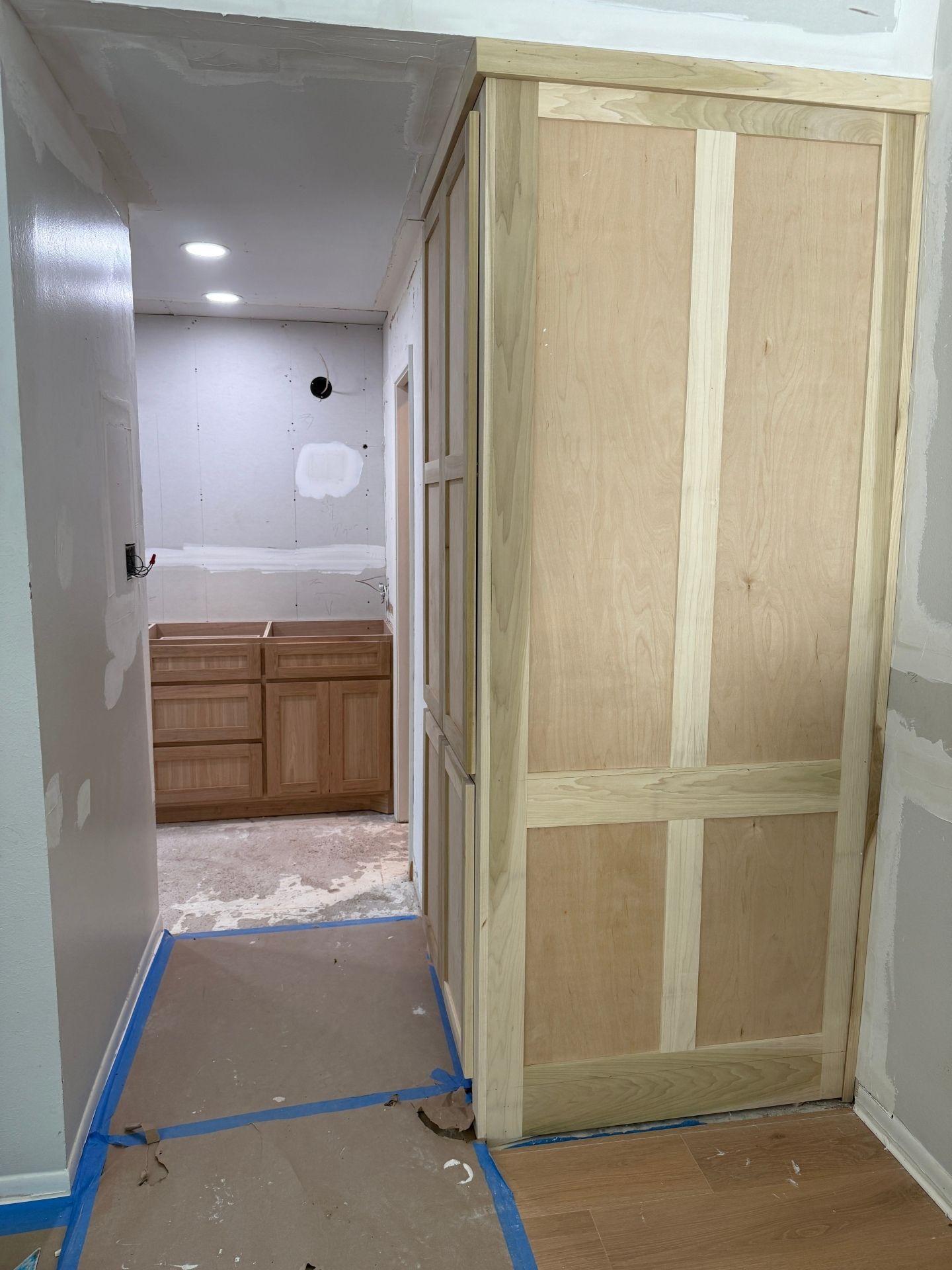 A hallway under construction with unfinished wood cabinetry and drywall, showing a vanity in the room beyond.