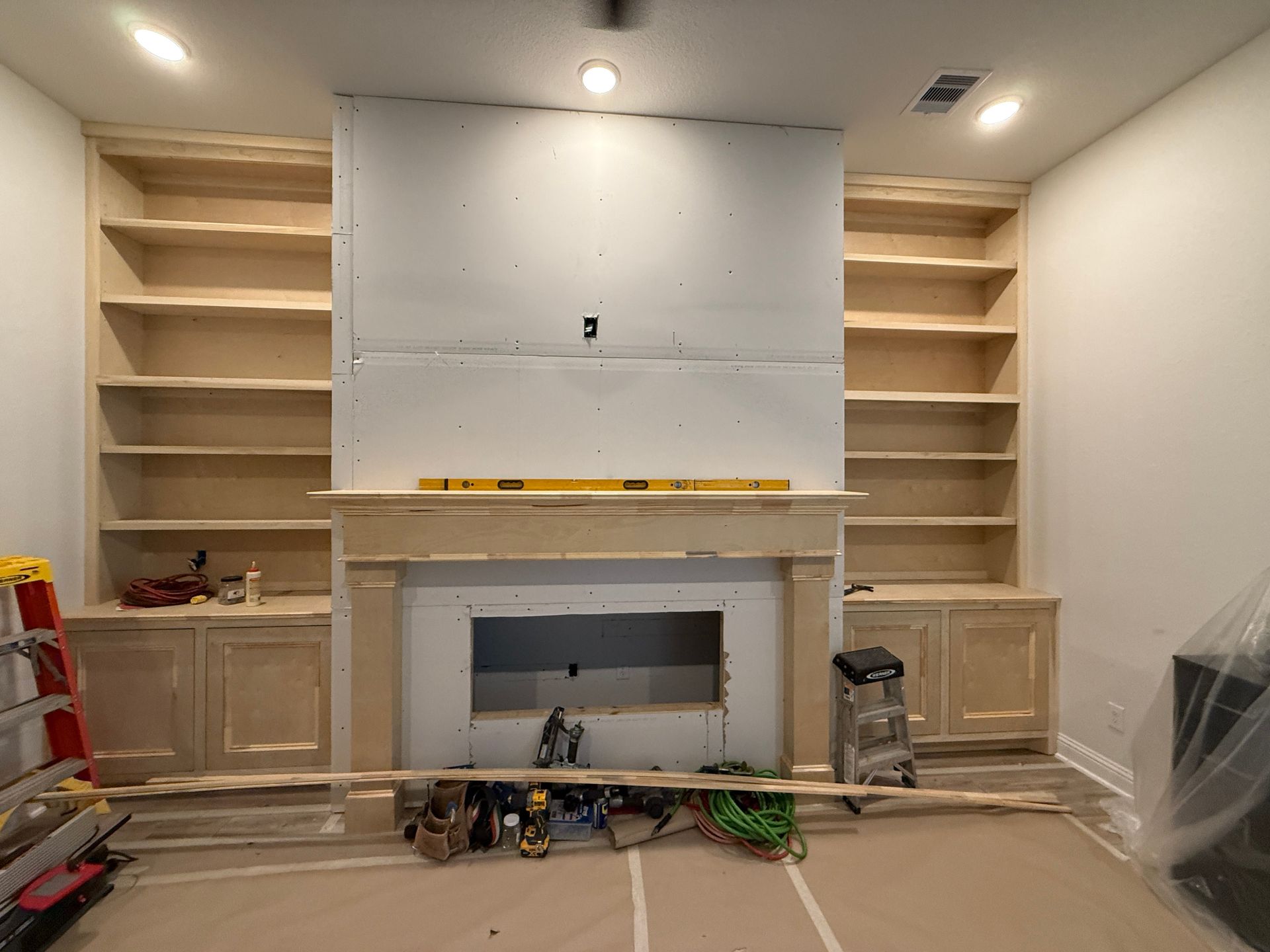 An unfinished fireplace flanked by custom built-in wooden shelving units in a room under construction.