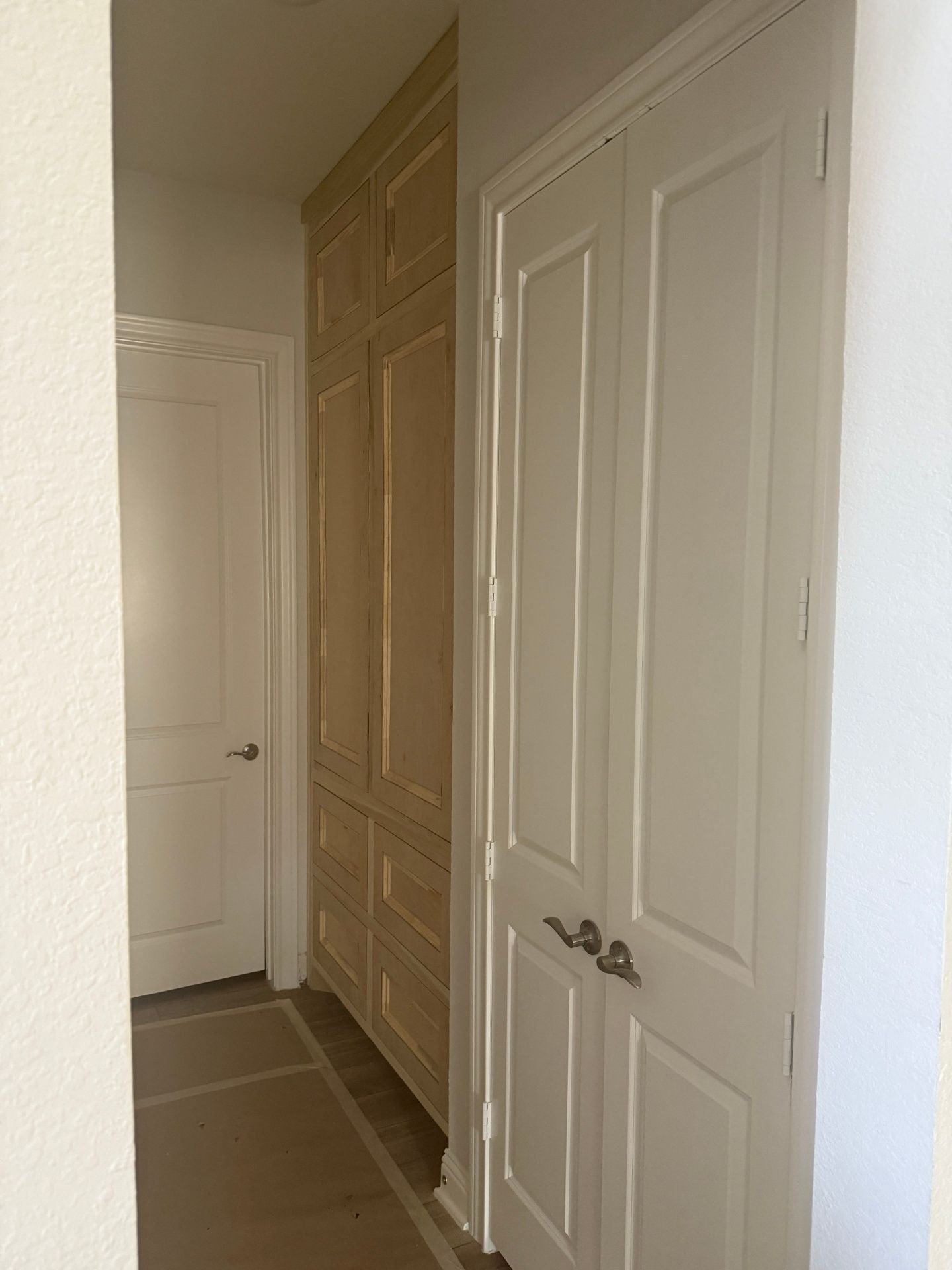A hallway featuring a light wood built-in cabinet on the left and white double doors on the right.