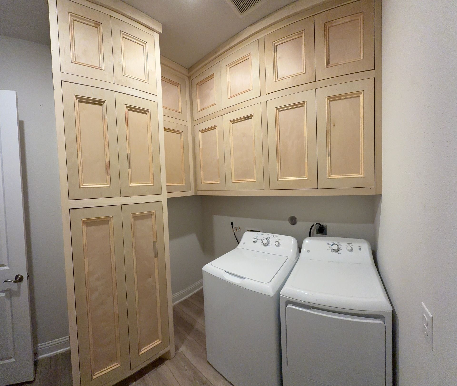Light wood laundry room cabinets mounted above white washer and dryer units.