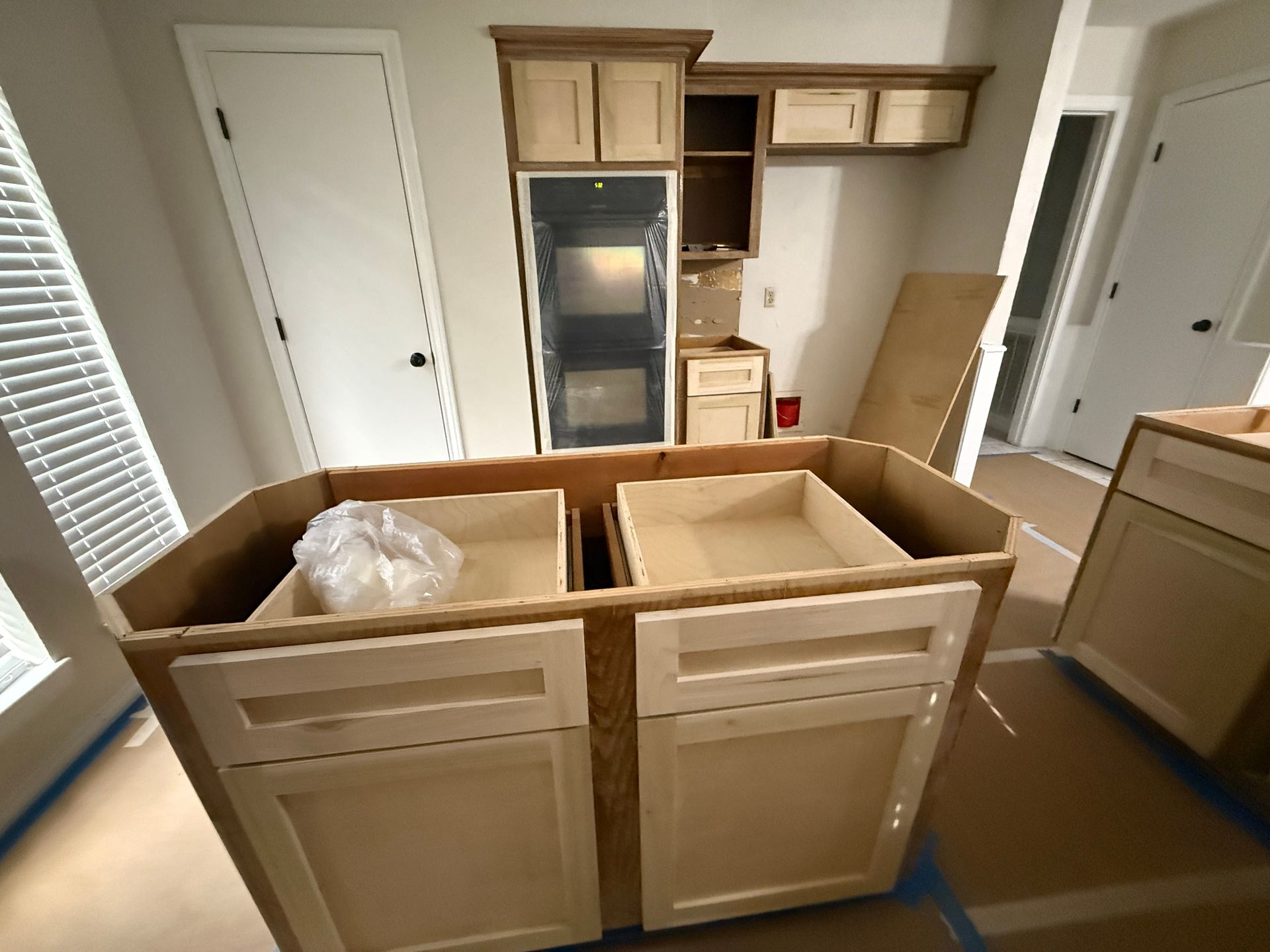 A kitchen under construction showing light wood cabinets and an island with open drawers on a floor covered with paper.