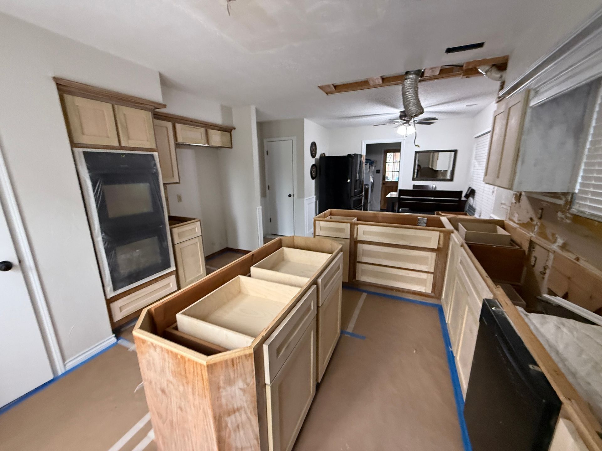 A kitchen undergoing renovation with light wood cabinets, an island with open drawers, and protected floors.