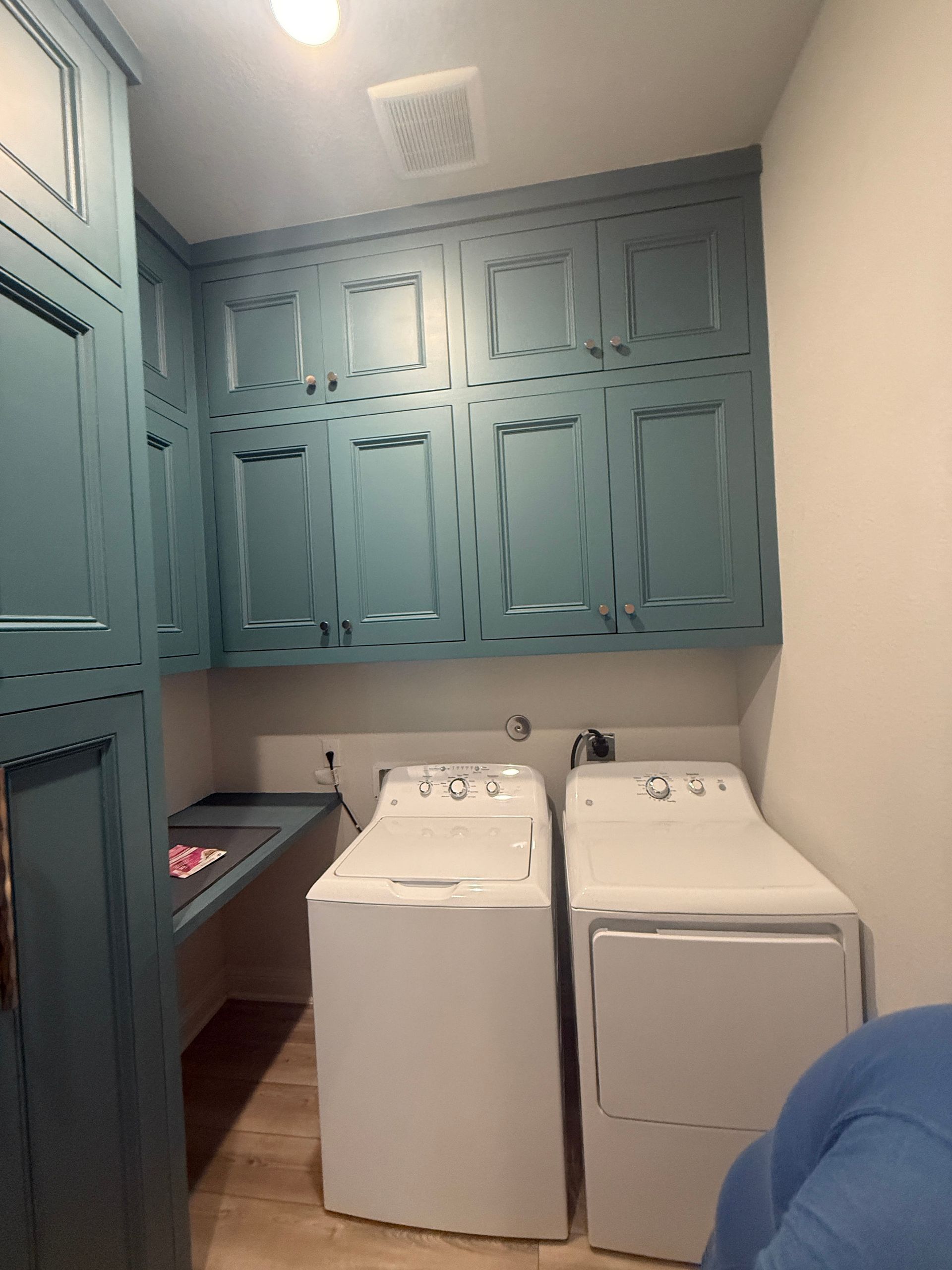 Laundry room with blue cabinets above white side-by-side washing machine and dryer, plus a small counter on the left.