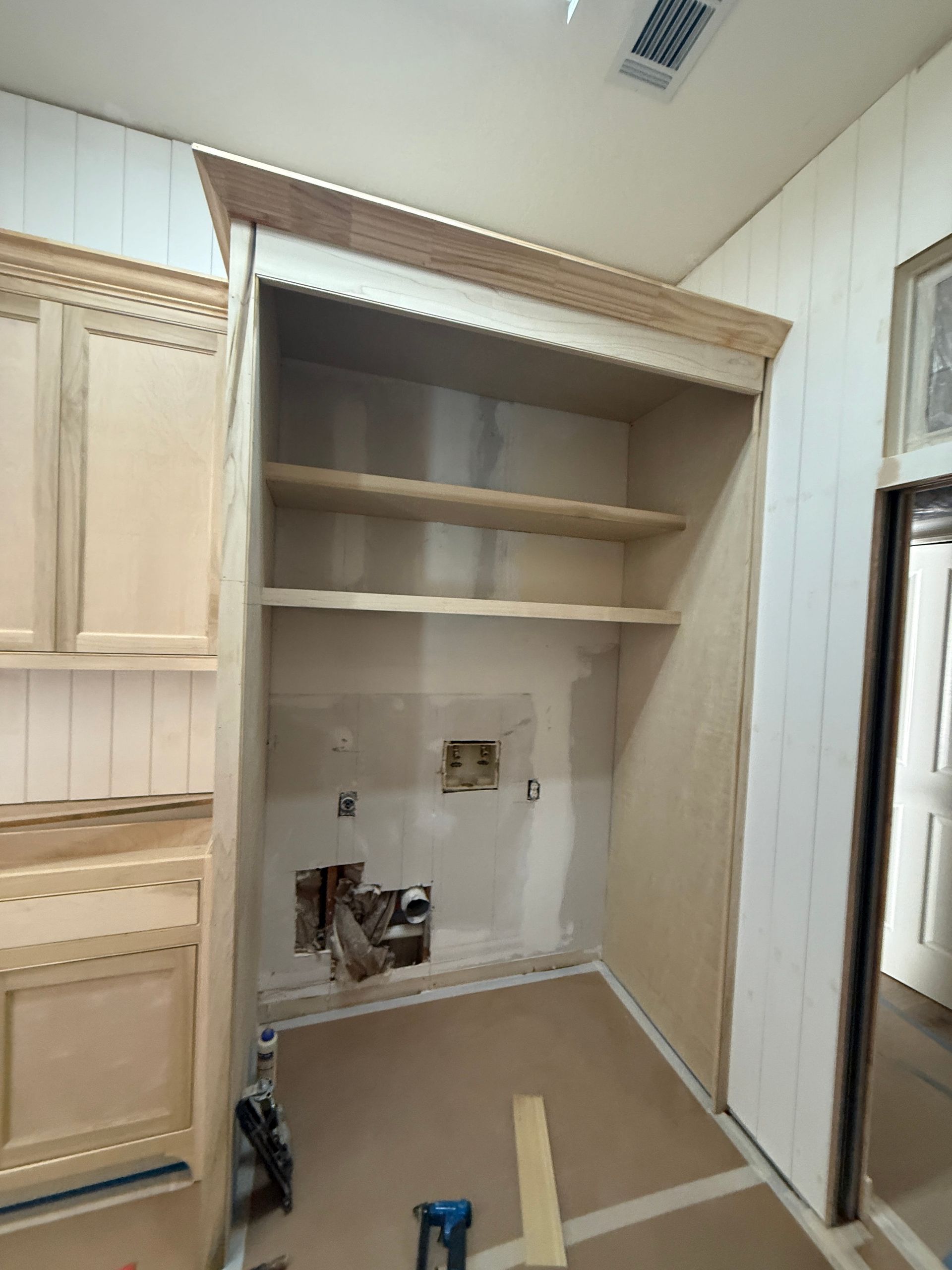 Unfinished kitchen cabinetry with a recessed space for appliances, open shelving, and exposed wall plumbing.