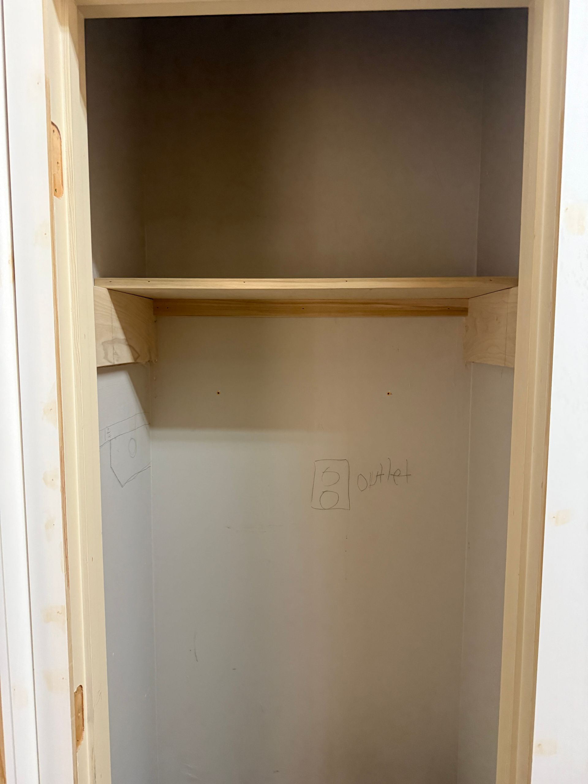 An empty, unfinished wall closet featuring a single wooden shelf supported by wooden brackets.